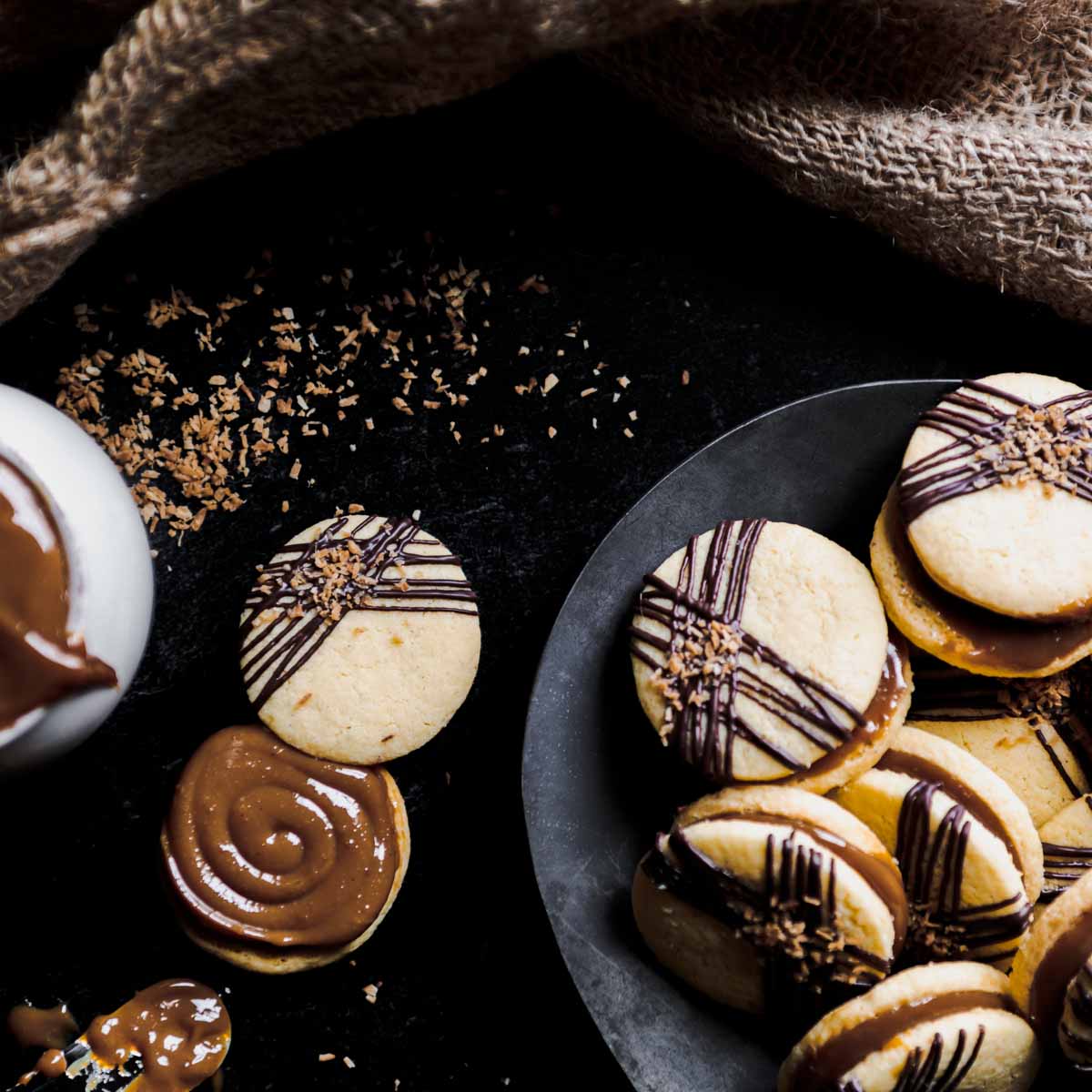 A plate full of Billionaire Alfajores with Toasted Coconut and a thick swirl of Dulce de Leche