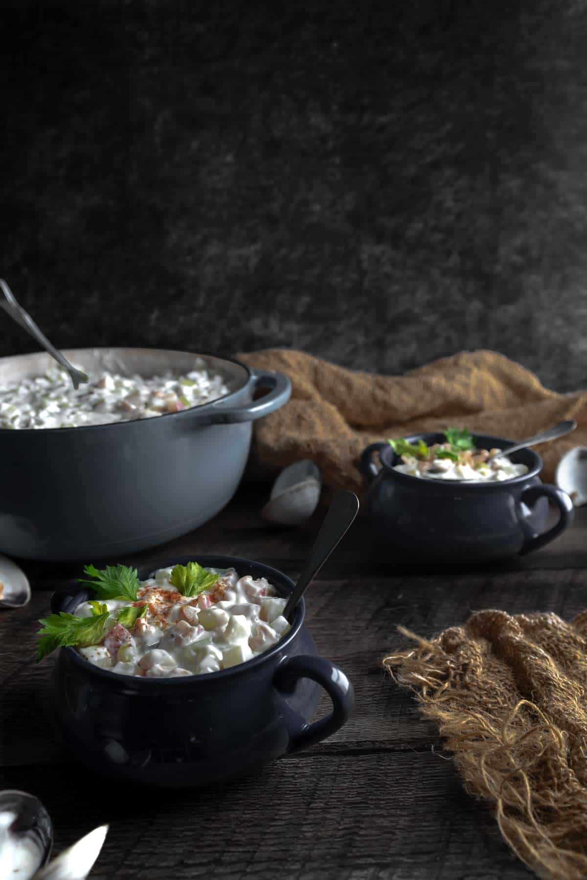 Bowls of Littleneck Clam Chowder made with Fresh Clams sitting next to opened clam shells and a big dutch oven full of chowder