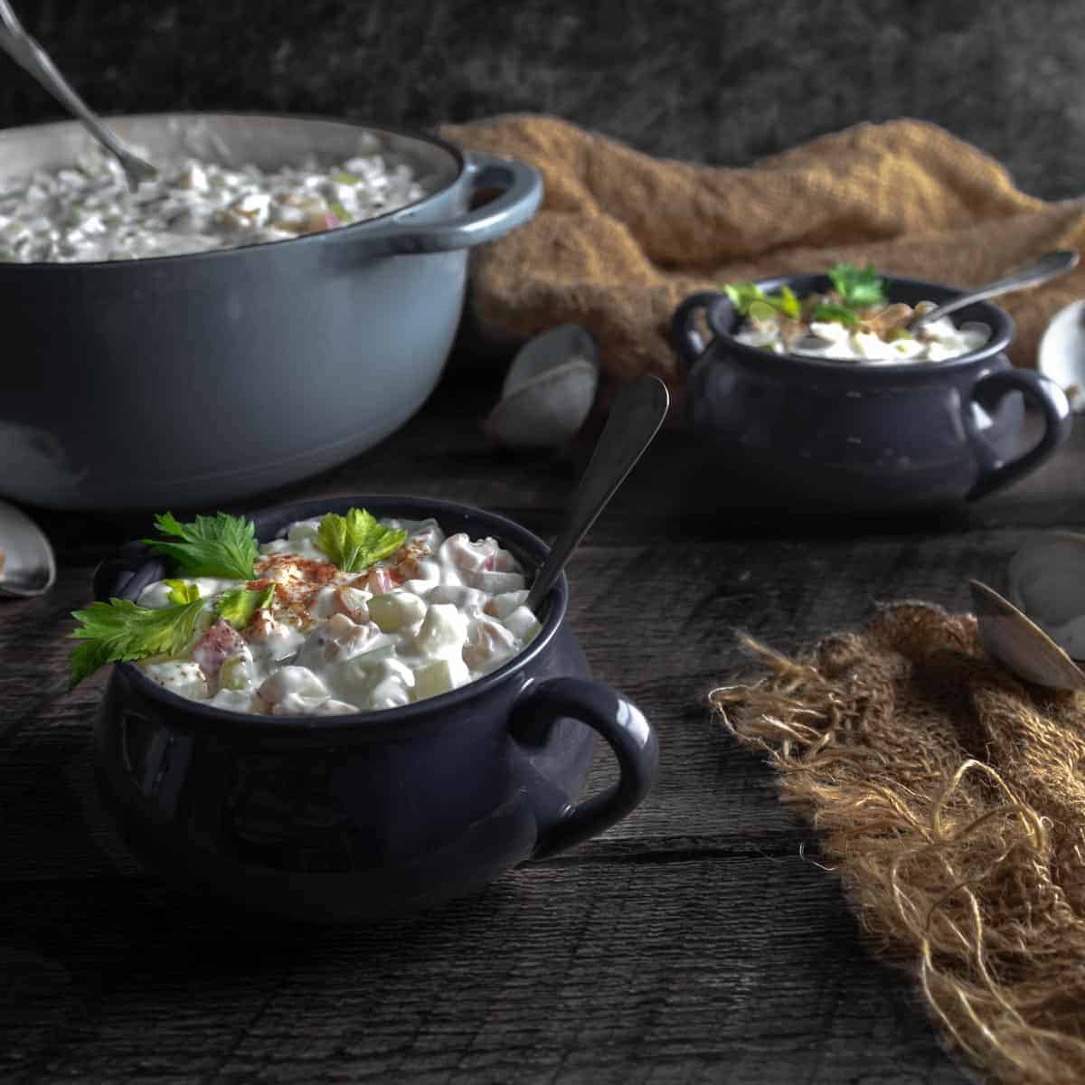 A big pot of Homemade Clam Chowder and two big bowls with spoons.