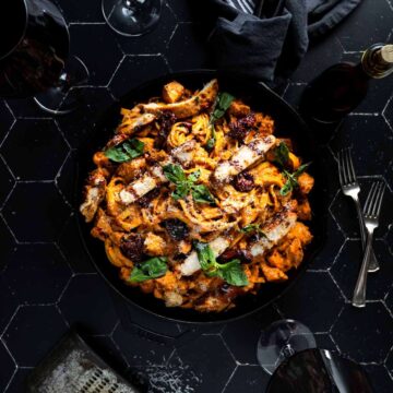 A big skillet of sun dried tomato chicken alfredo garnished with balsamic glaze and fresh basil