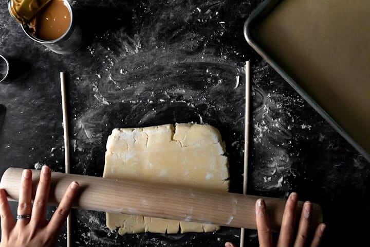 Cookie dough surrounded by quarter inch dowels being rolled with a rolling pin to the perfect thickness