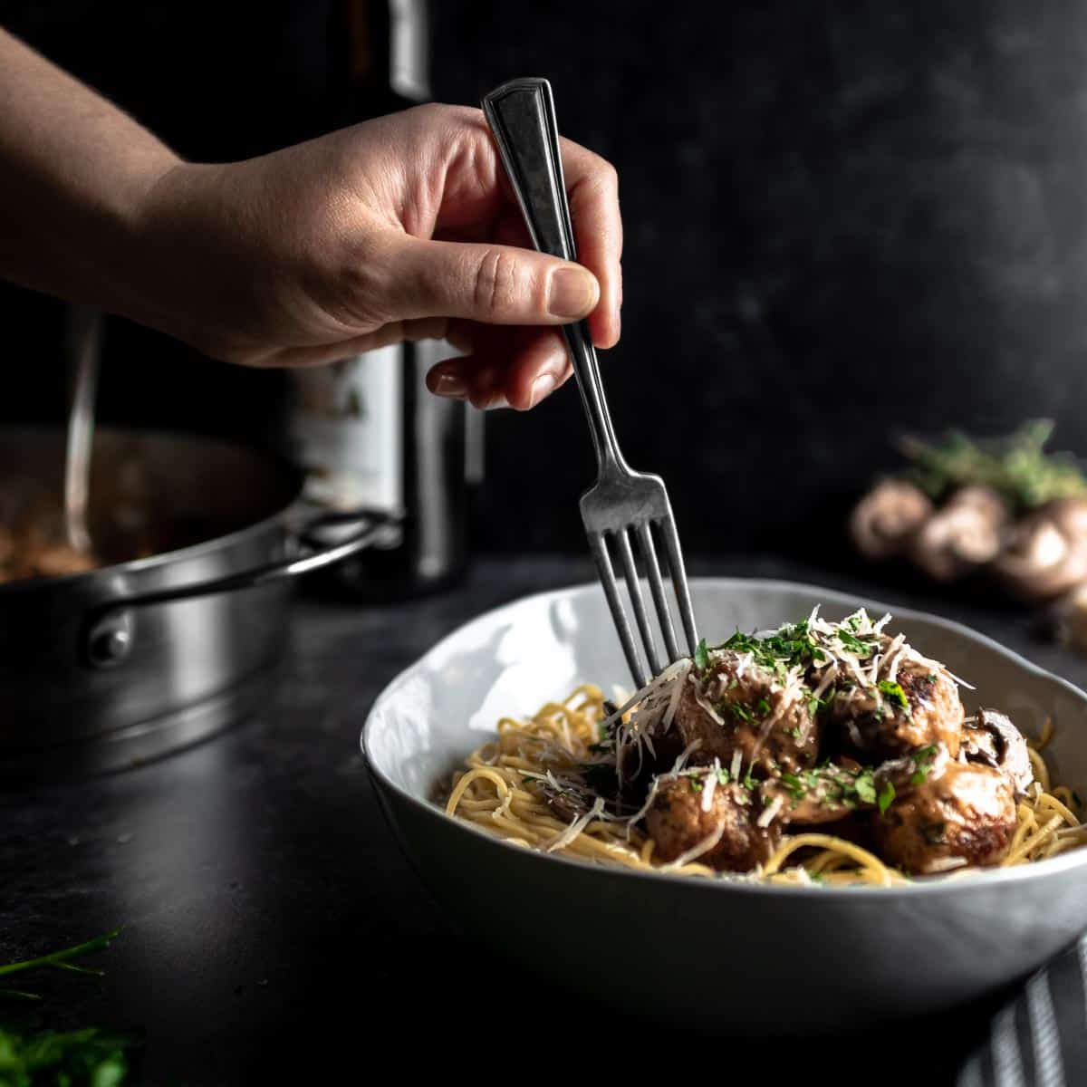 A fork going into a big bowl of spaghetti and meatballs in marsala sauce