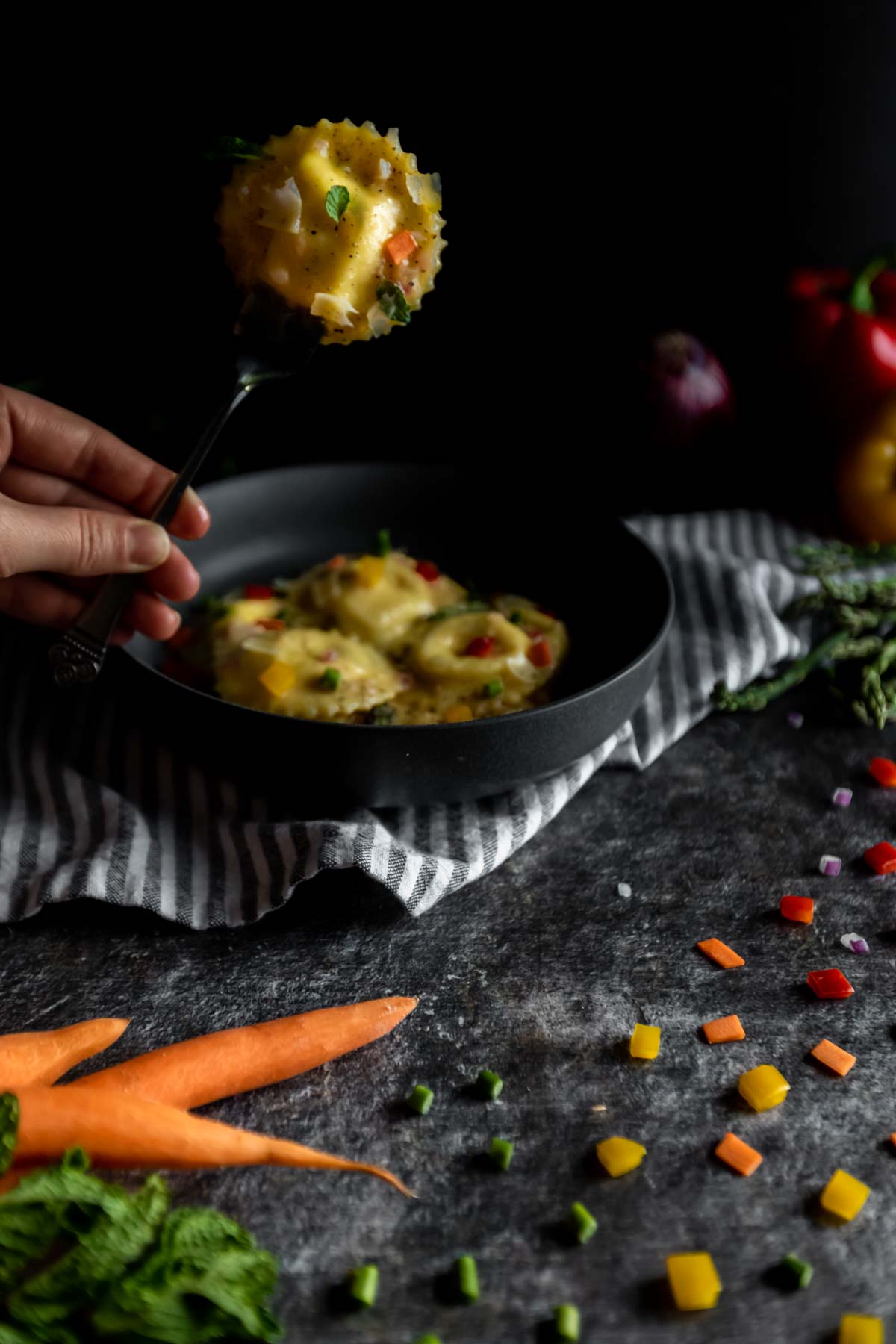 A whole ravioli on a fork surrounded by “confetti” vegetables