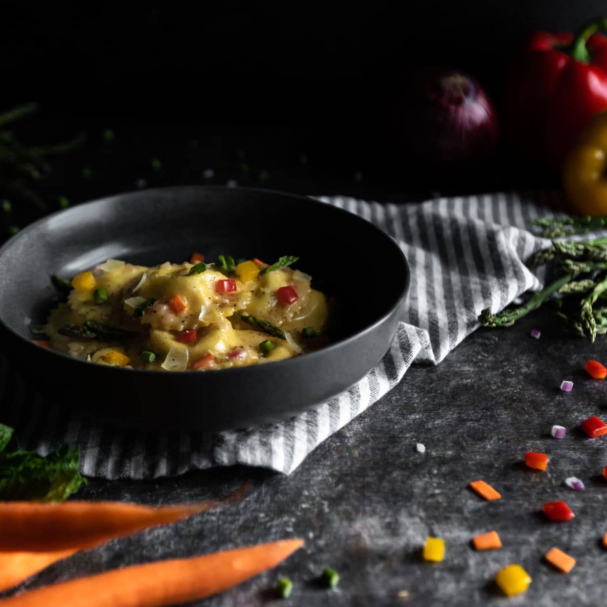 A bowl of Ravioli Primavera surrounded by Spring vegetables