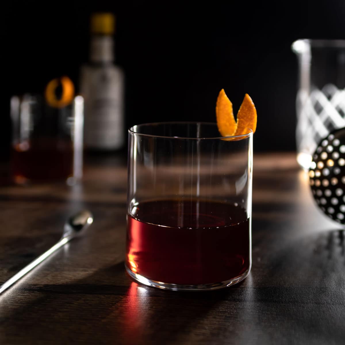 amaro old fashion in glass with orange twist and a spoon next to it.