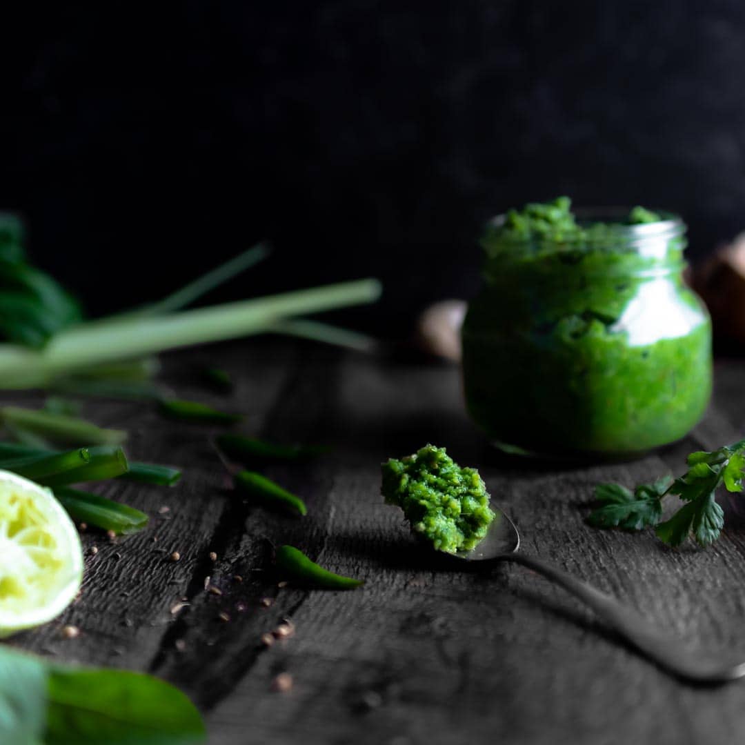 a spoonful of homemade green curry paste next to a full jar, Thai Chile peppers, lemongrass, basil, lime and coriander