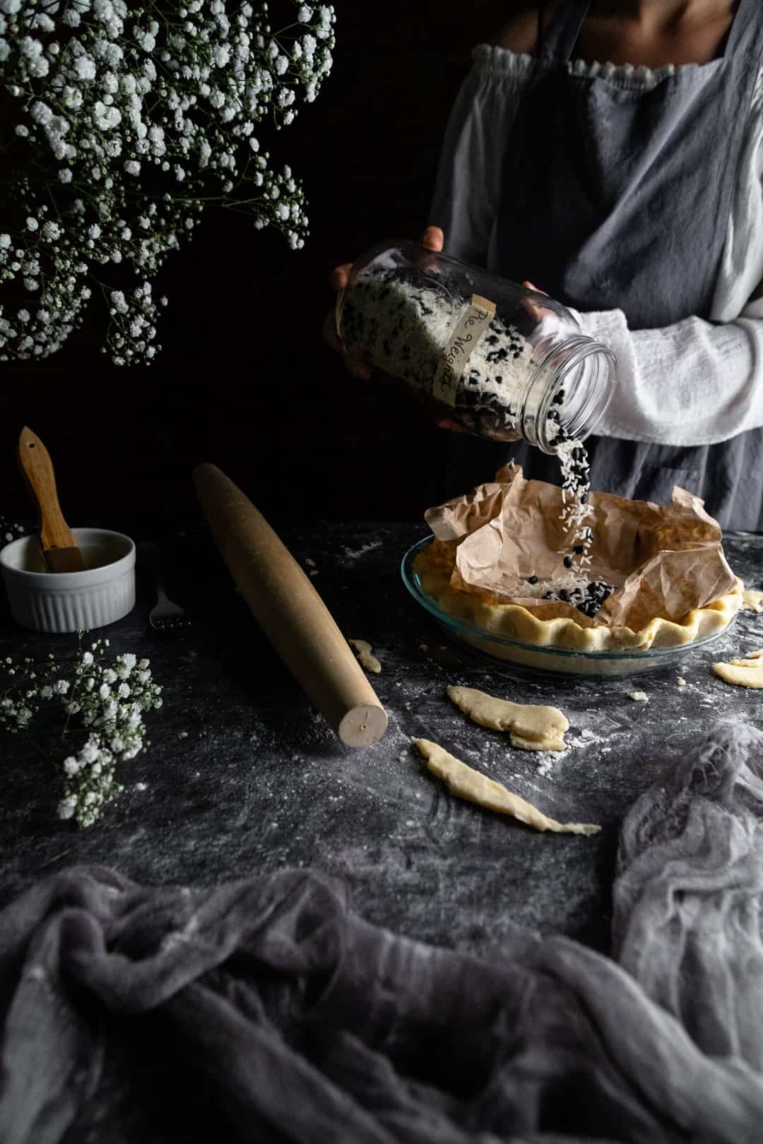 A woman pouring dried rice and beans from a jar into the coffee-filter lined unbaked pie crust. She is preparing the pie crust for blind baking.