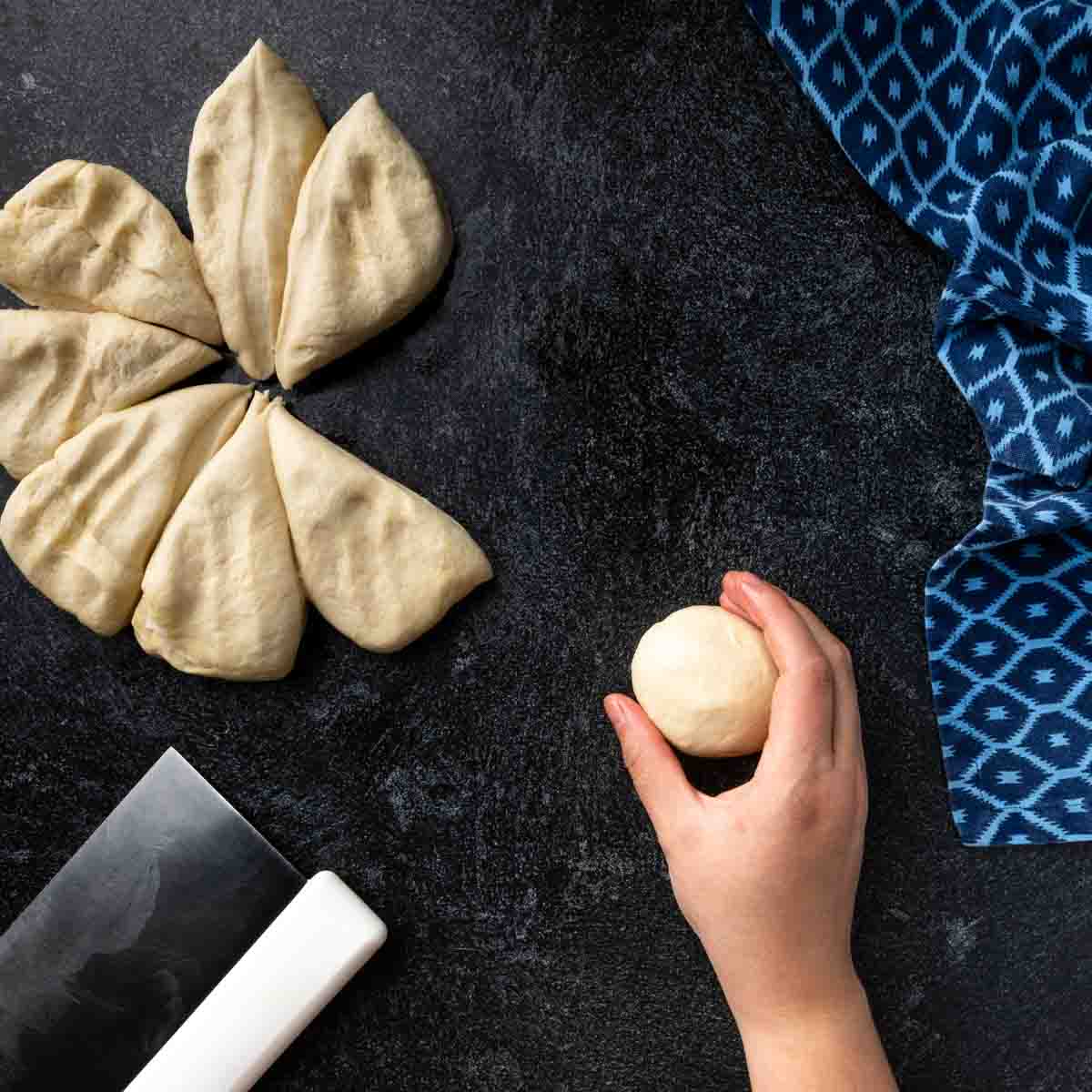 A flattened ball of dough cut into 8 wedges with one being shaped into a ball. 