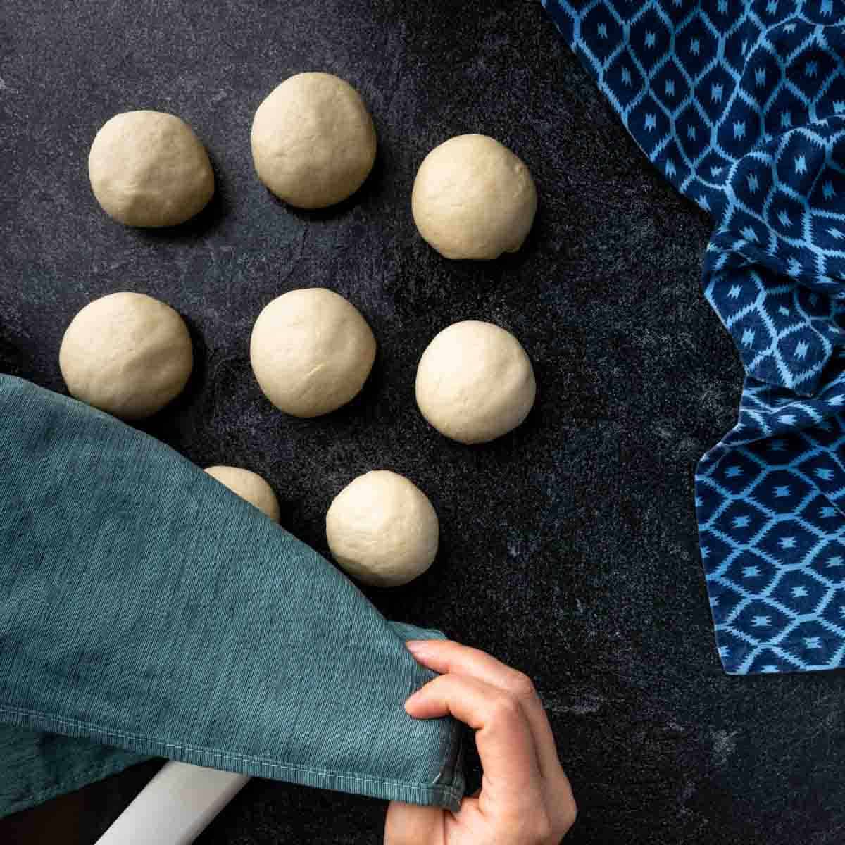 Eight balls of pita dough being covered by a kitchen towel. 