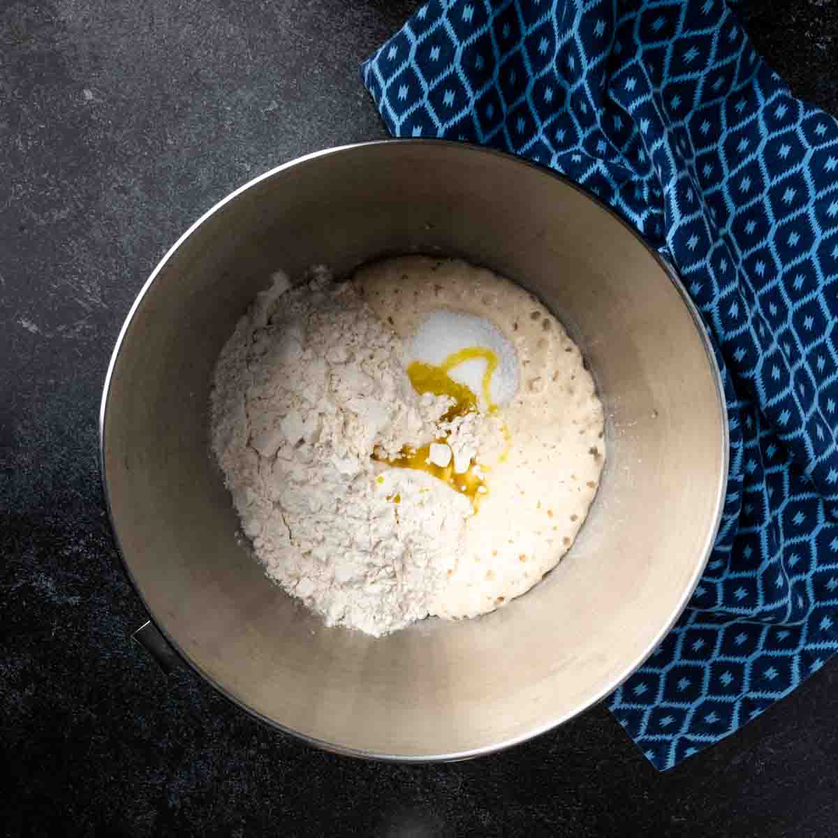 The bowl of a stand mixer filled with ingredients for pita bread dough. 