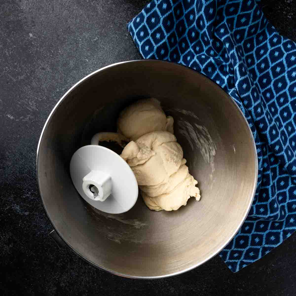 Pita dough clung to a dough hook in the bowl of a stand mixer. 