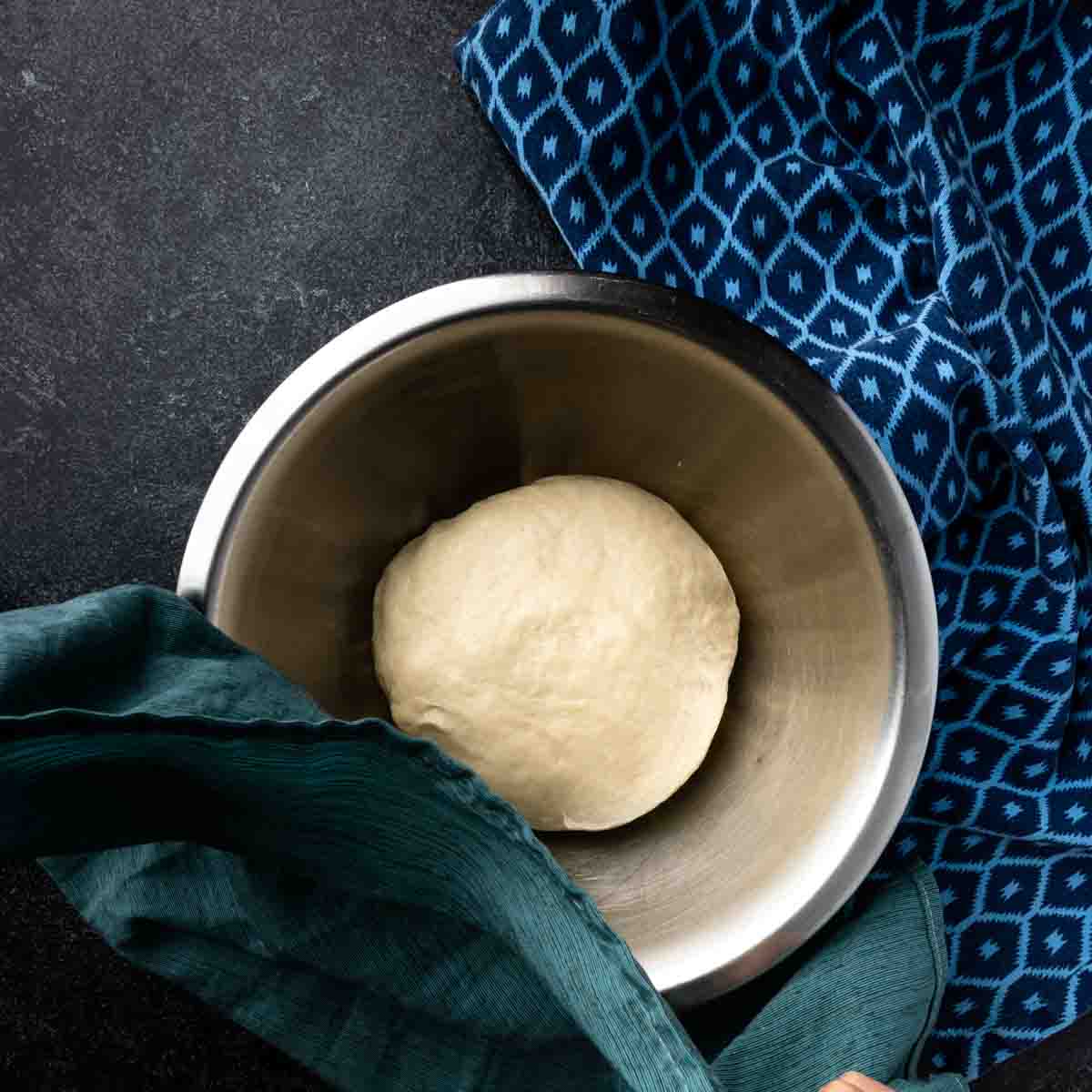 A round ball of pita dough in an oiled mixing bowl. 