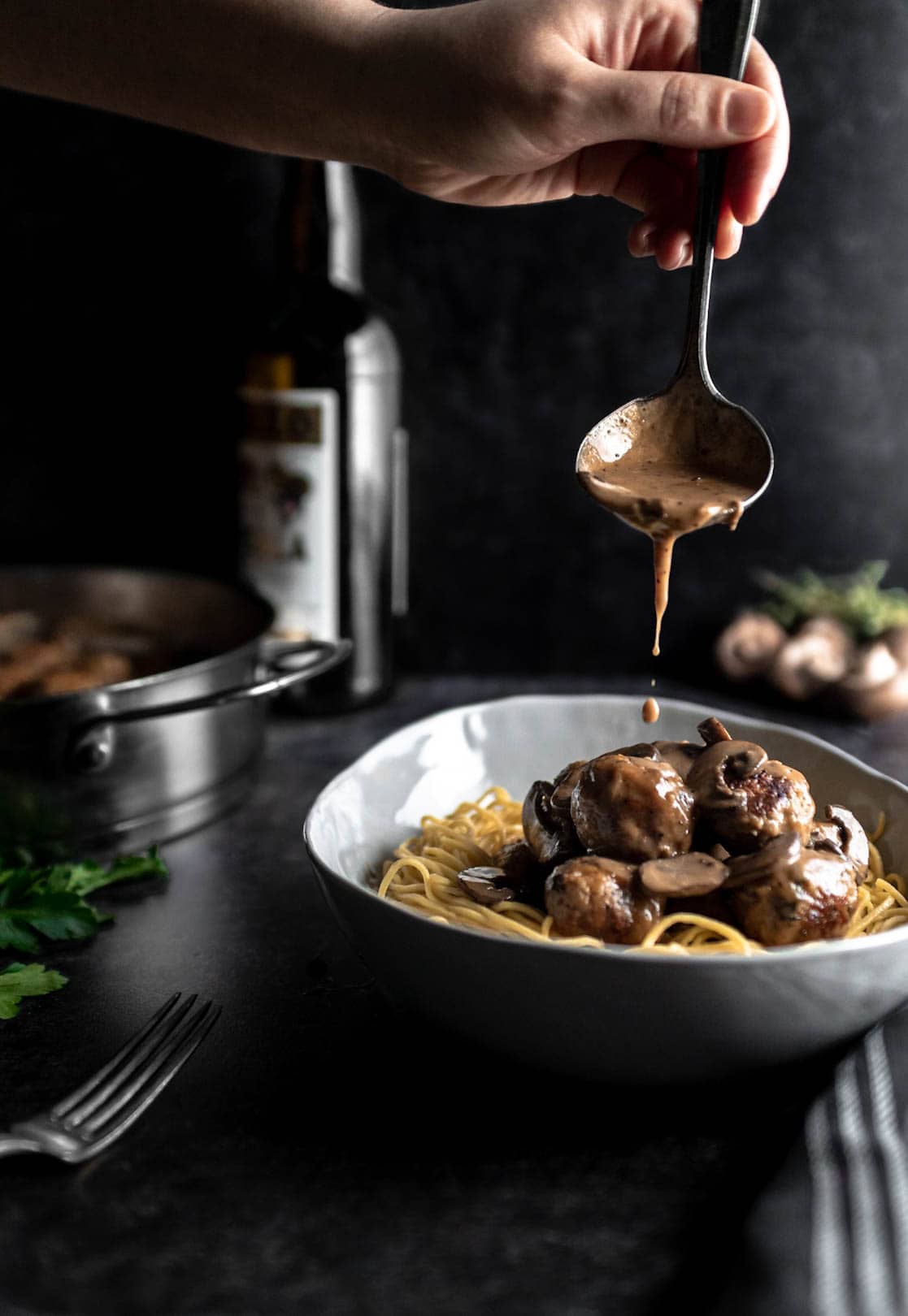 a ladle pouring marsala sauce over spaghetti and meatballs