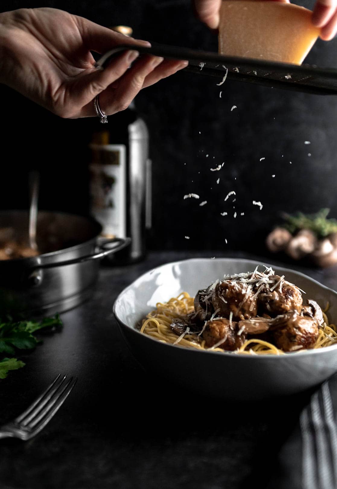 shredding Parmesan cheese over Chicken Marsala Meatballs