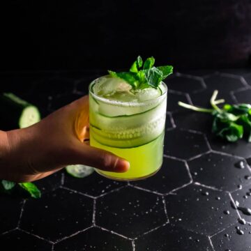 A hand holding a cucumber mojito