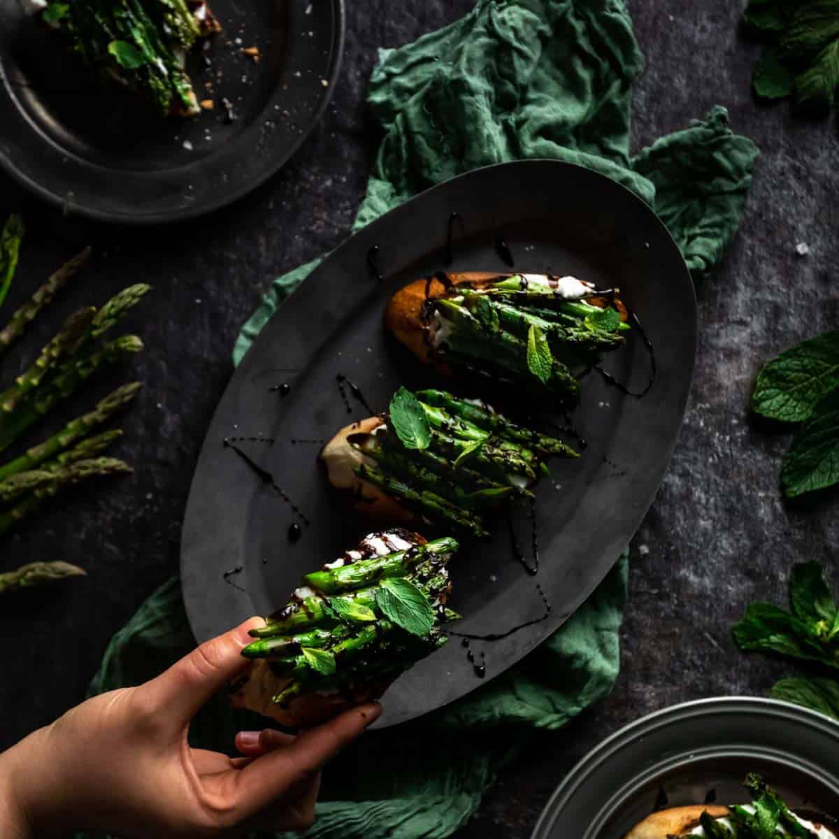 A hand reaching for a Whipped Ricotta & Grilled asparagus toast