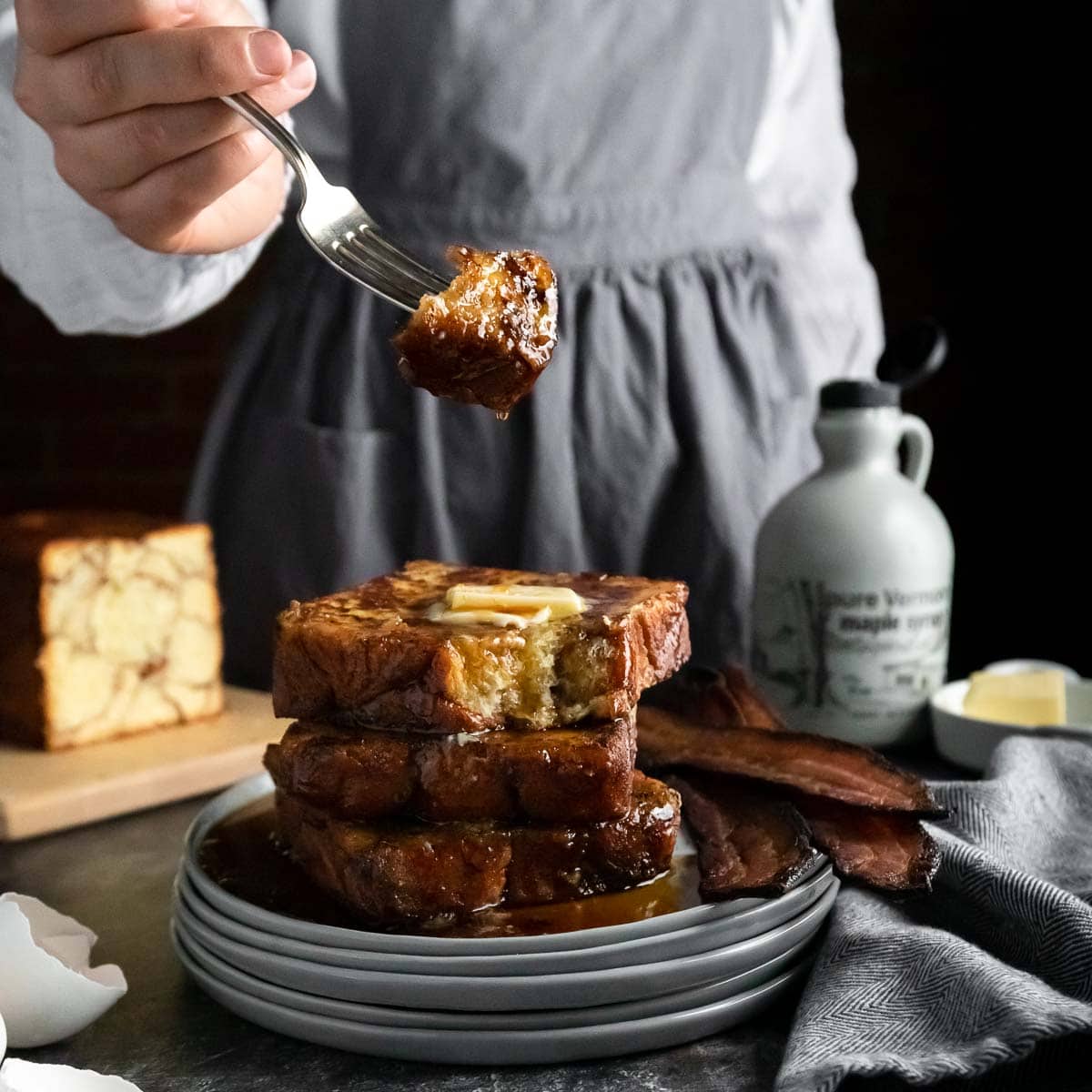 A bite of Monkey Bread French Toast on a fork being held above a tall stack of French toast