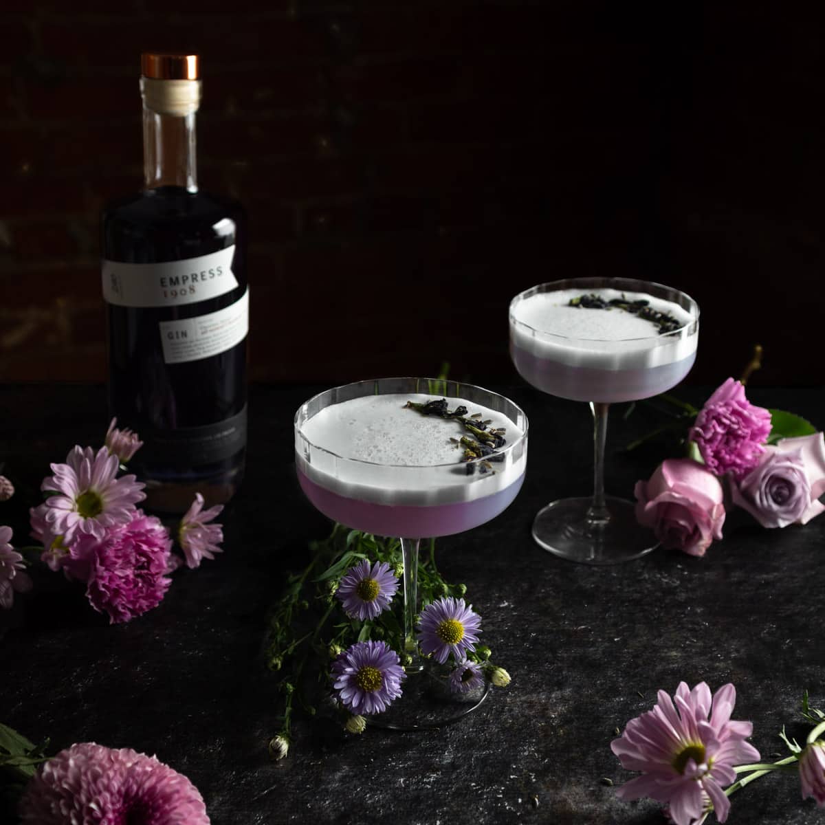 Empress 1908 Gin sour Cocktails surrounded by fresh purple flowers and a bottle of Empress gin