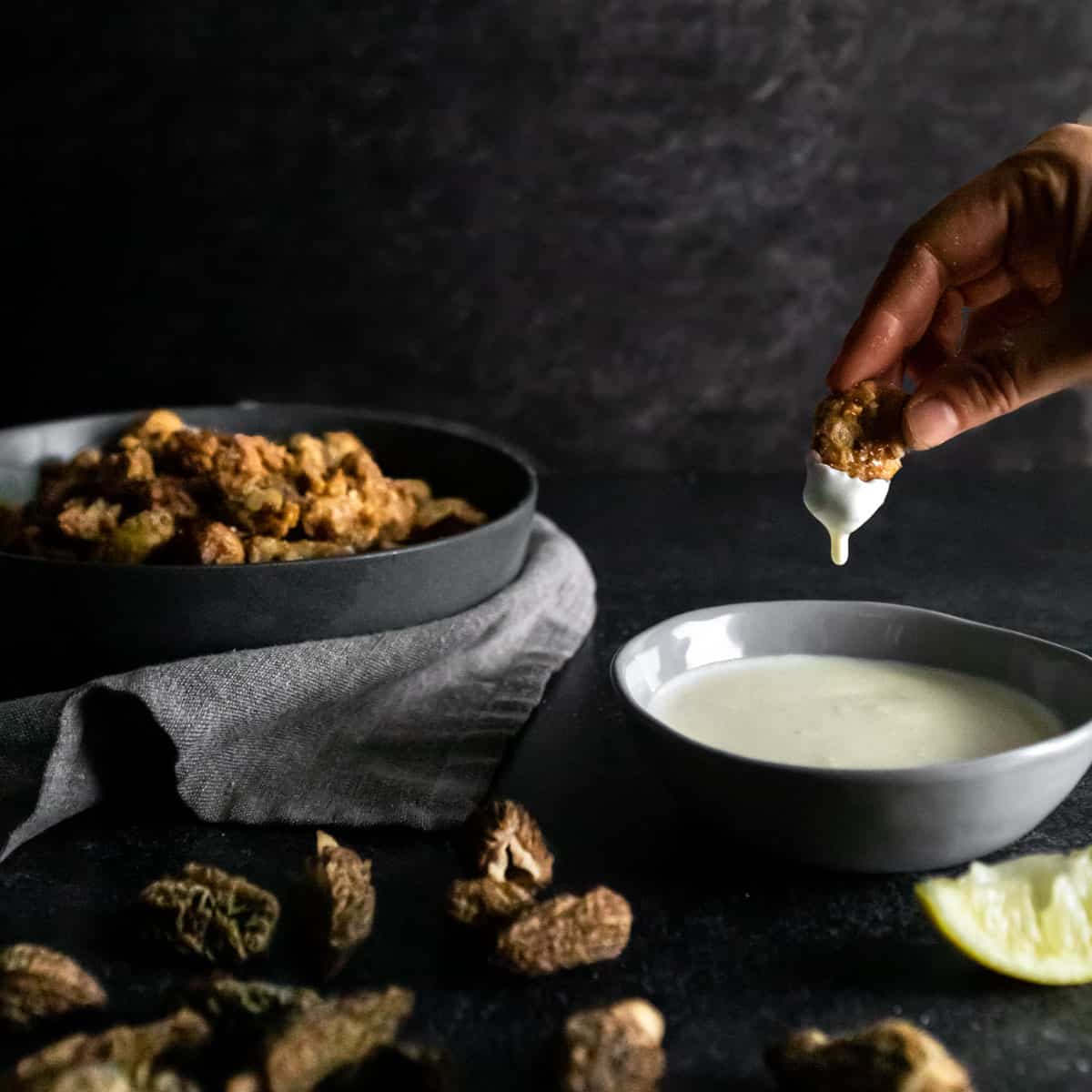 a fried morel mushroom being dipped into lemon Crema