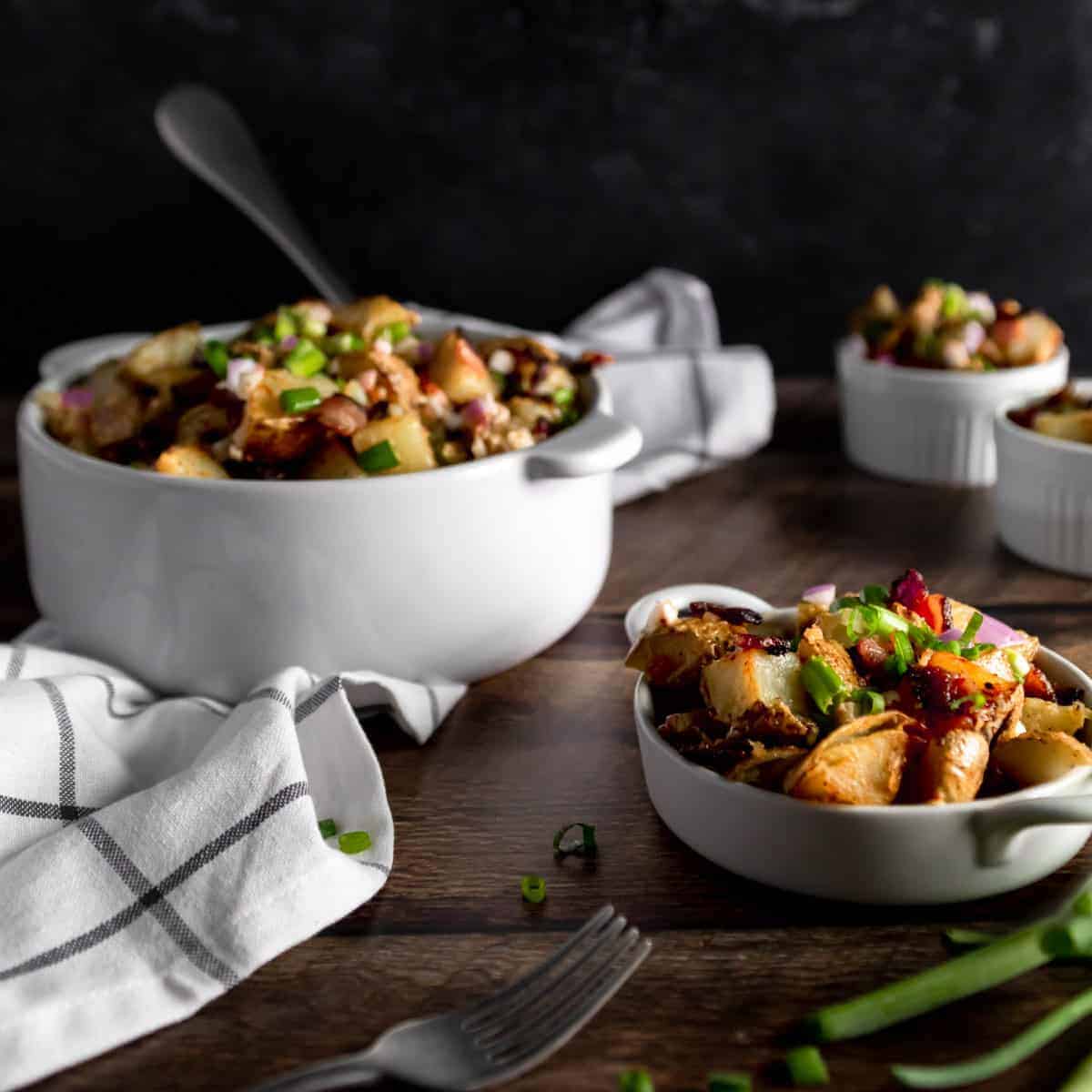 A big bowl with fried potato salad with bacon and two servings