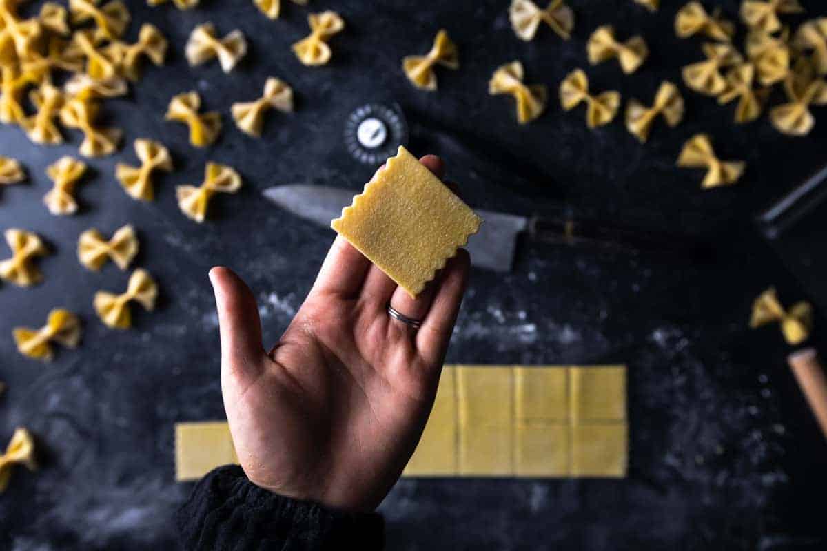 a hand holding up a square with parallel fluted edges to use for farfalle pasta