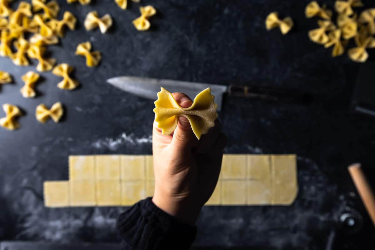 a hand pinching the center seal of a square of pasta dough