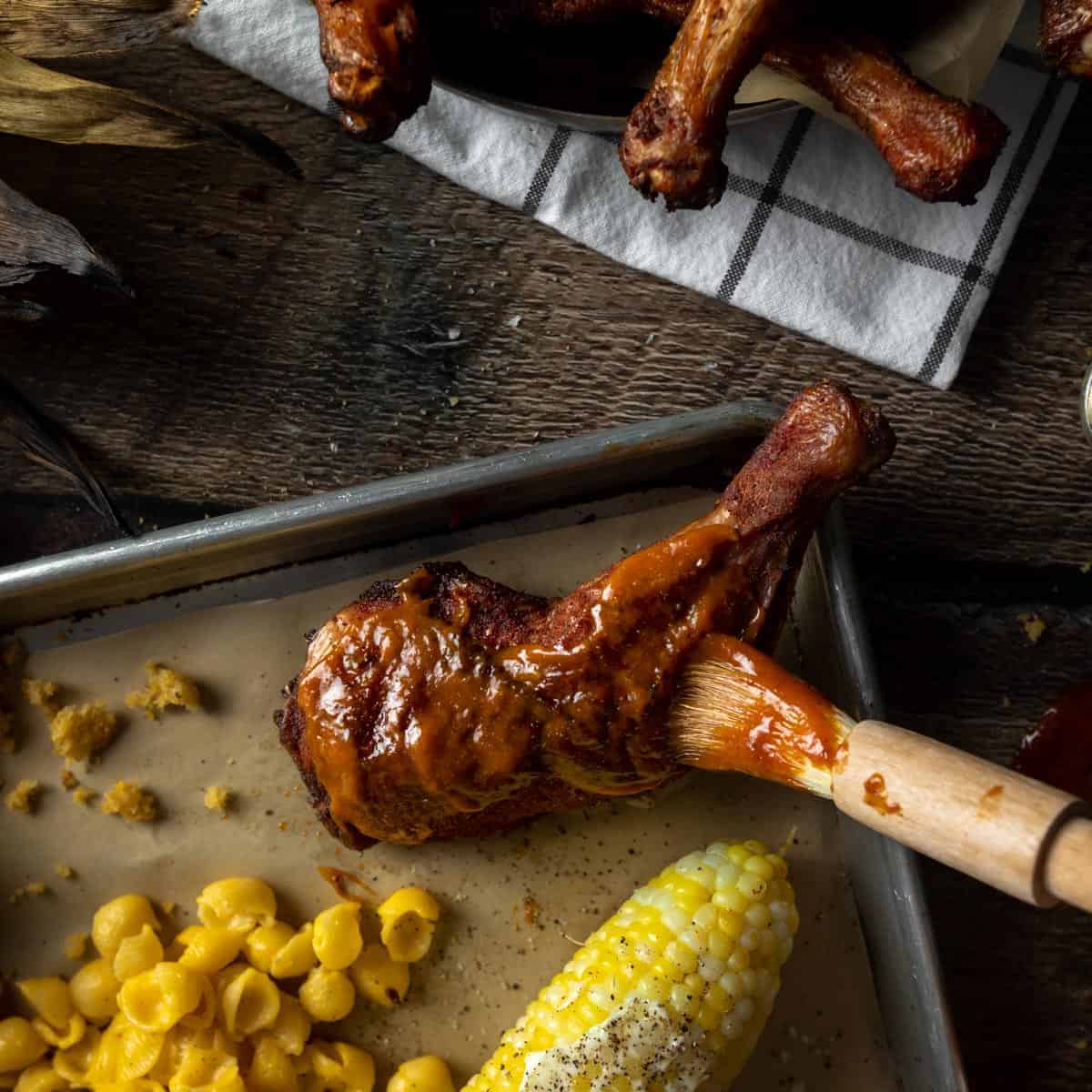 A tray of BBQ food including a smoked chicken leg being glazed with a brush of Apricot BBQ Sauce