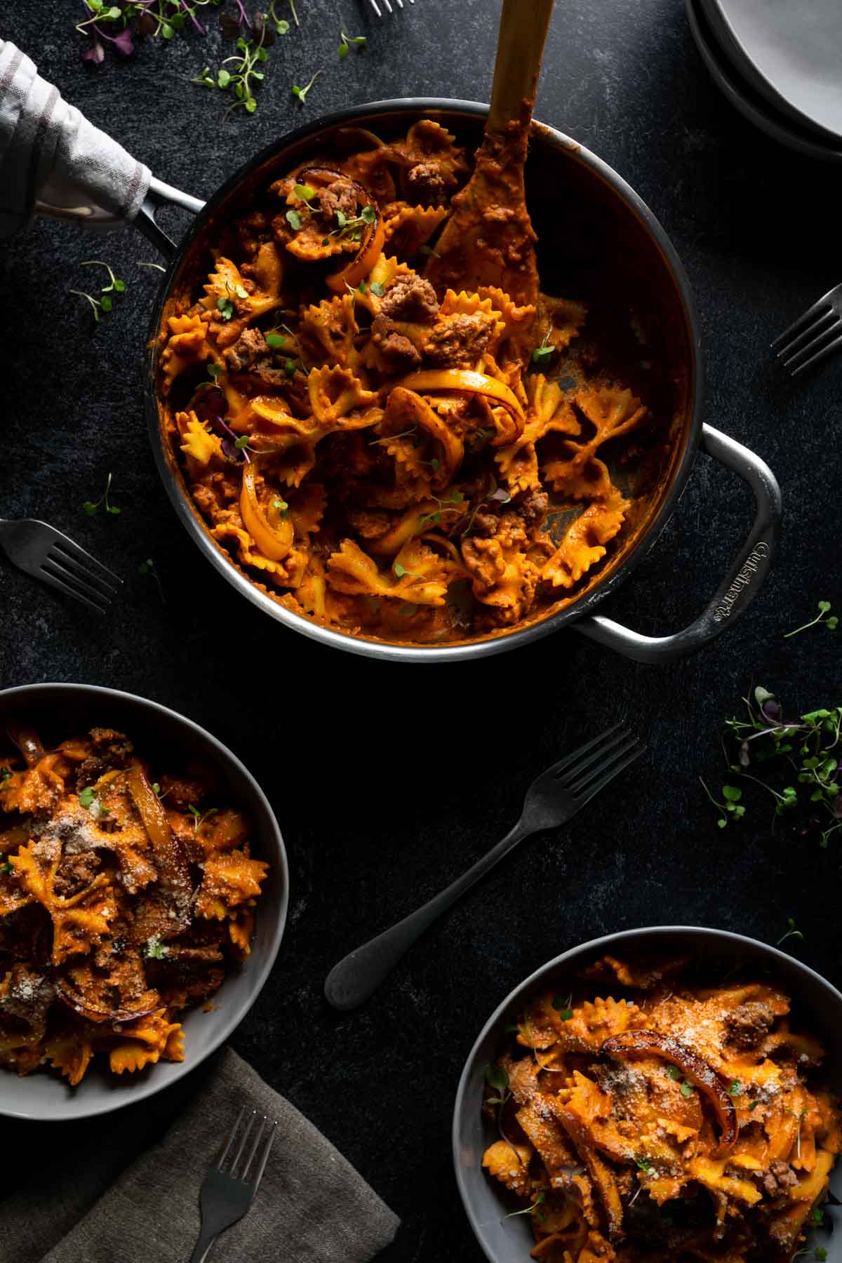 A big skillet and two bowls full on tomato based cajun pasta with andouille sausage