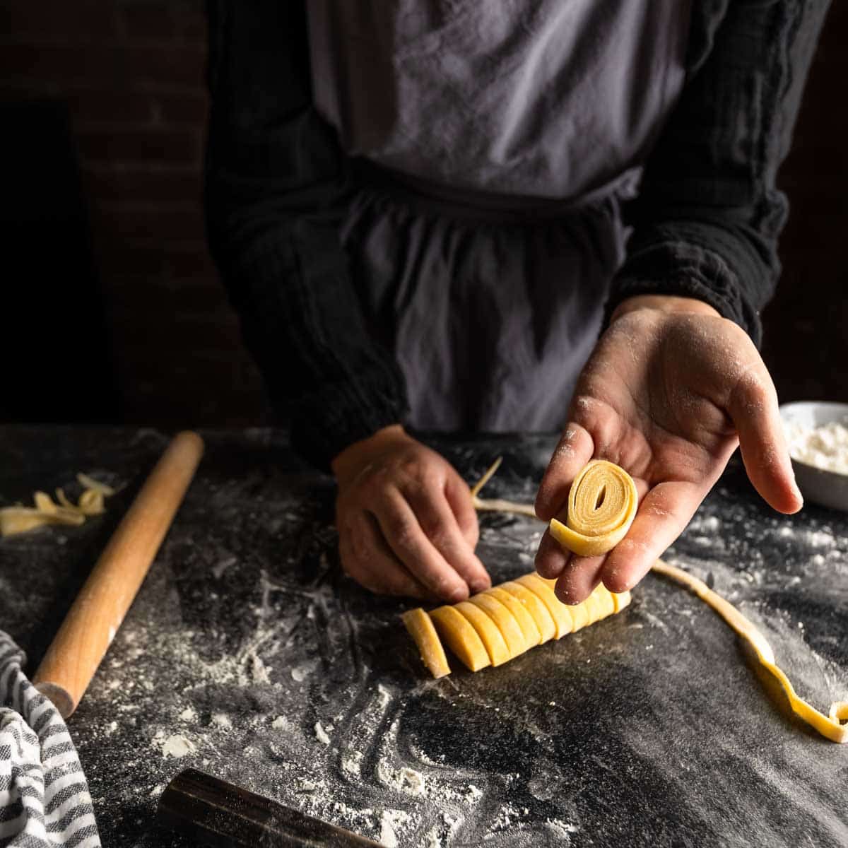 A woman holding a spiral of freshly cut fettuccine pasta in her hand.