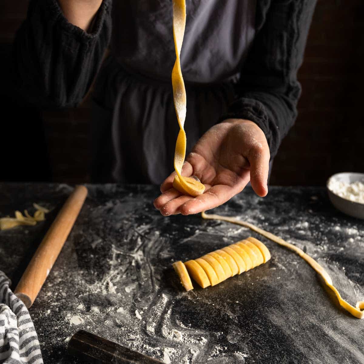A woman unraveling a little ribbon of fettuccine pasta.