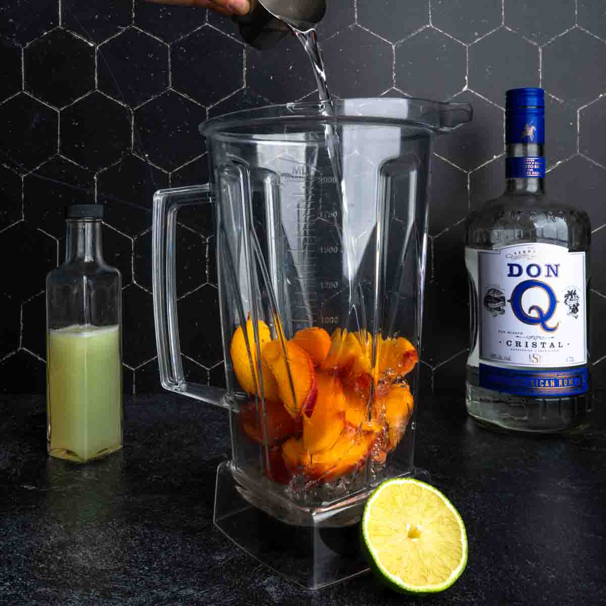 Pouring rum into a blender of frozen peaches. 