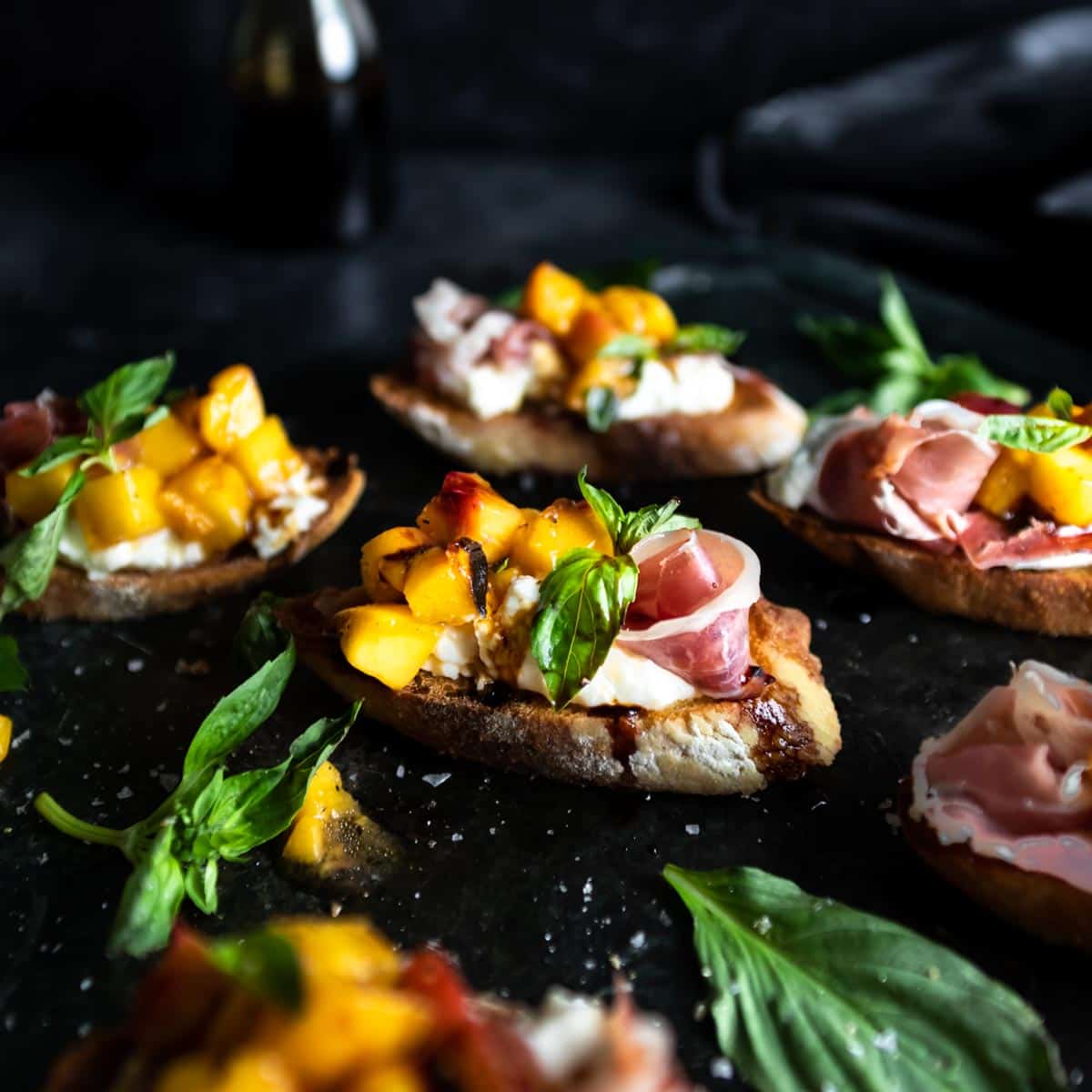 A close up shot a a grilled peach and Burrata Bruschetta with a prosciutto rose and fresh basil