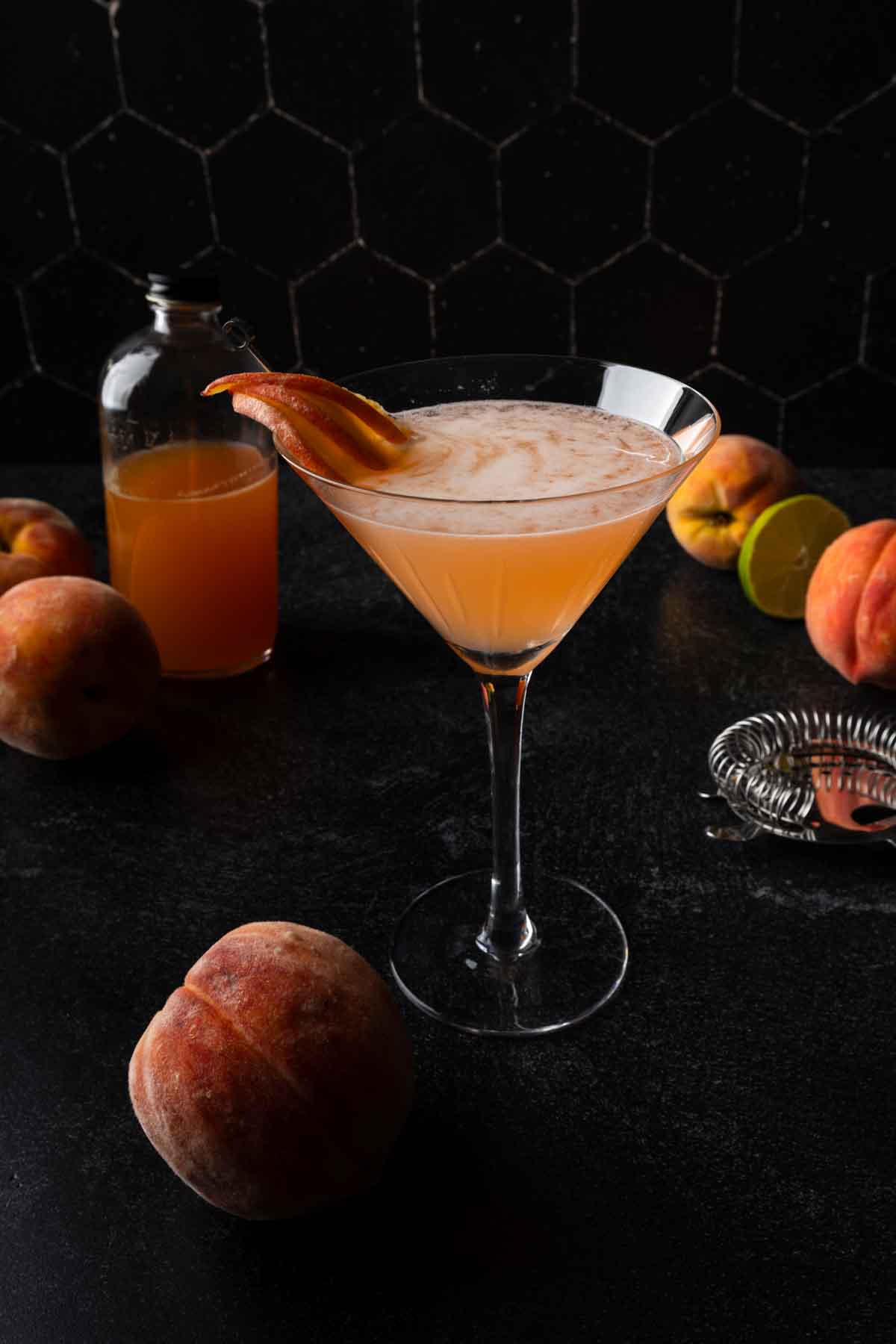 A peach daiquiri in a martini glass surrounded by fresh peaches. 