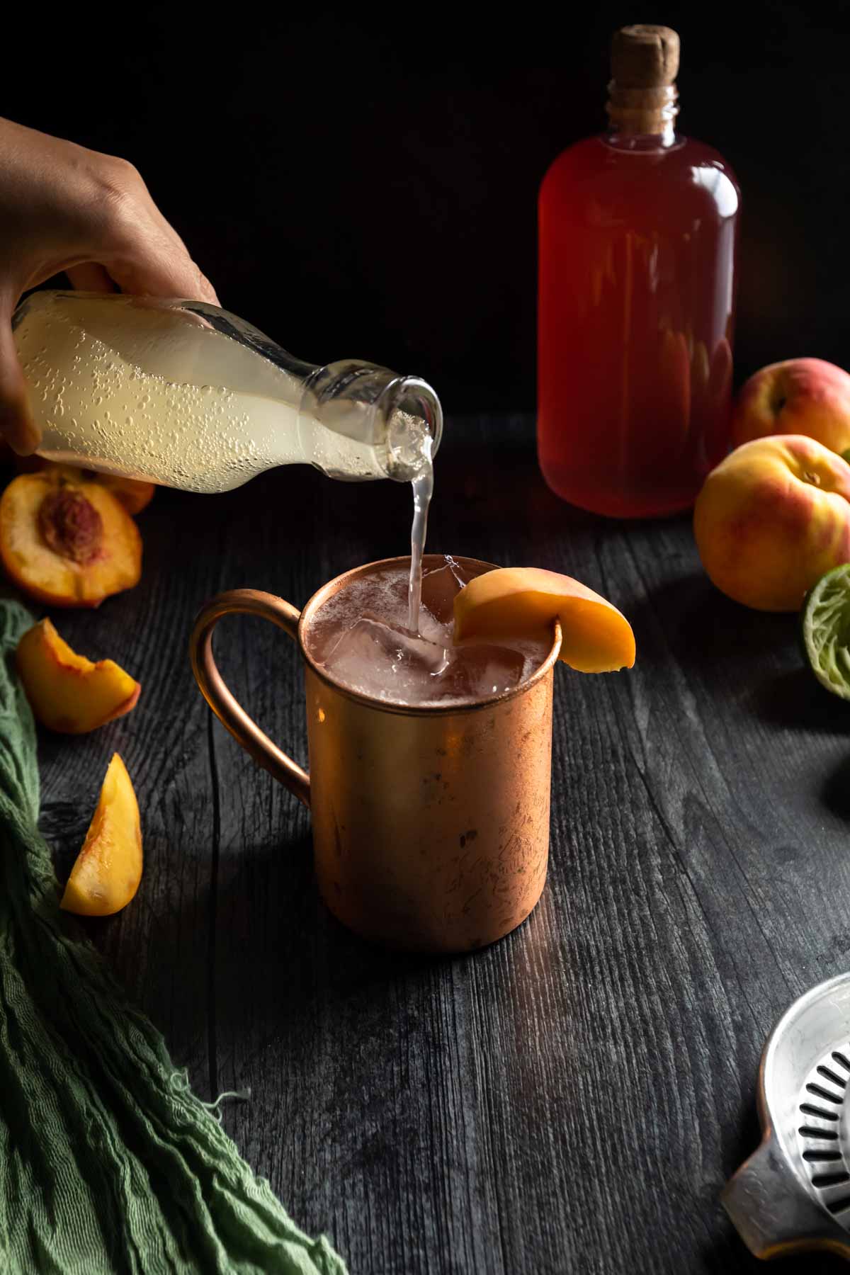 Topping a copper mug Peach Moscow Mule with a pour of ginger beer