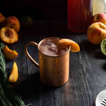 A peach Moscow mule in a copper mug garnished with a fresh peach slice