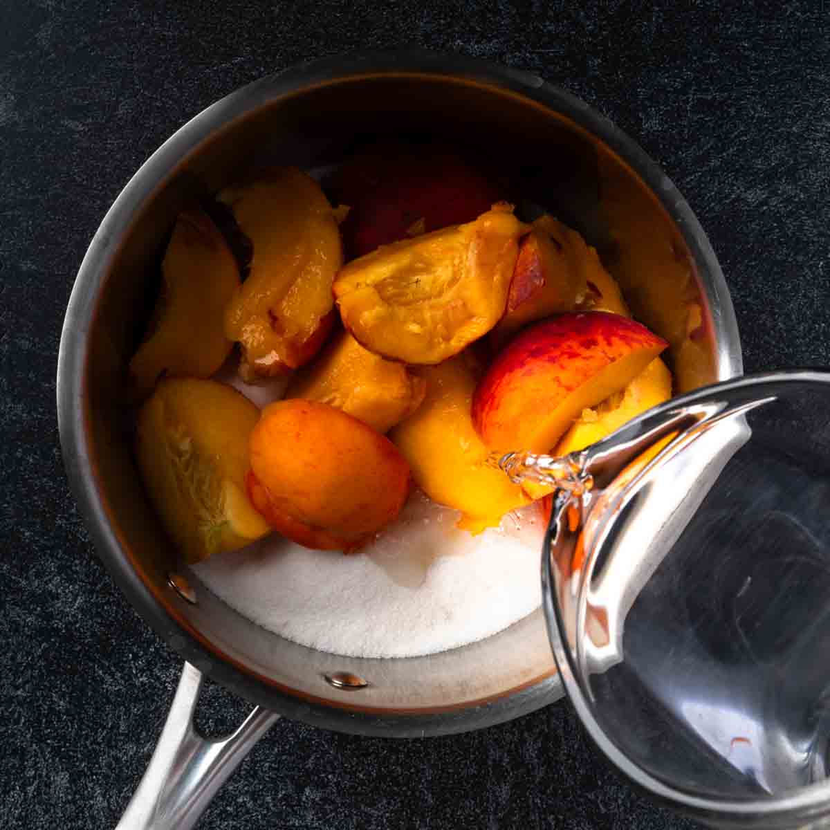 Pouring water into a sauce pot filled with white sugar and fresh peaches. 