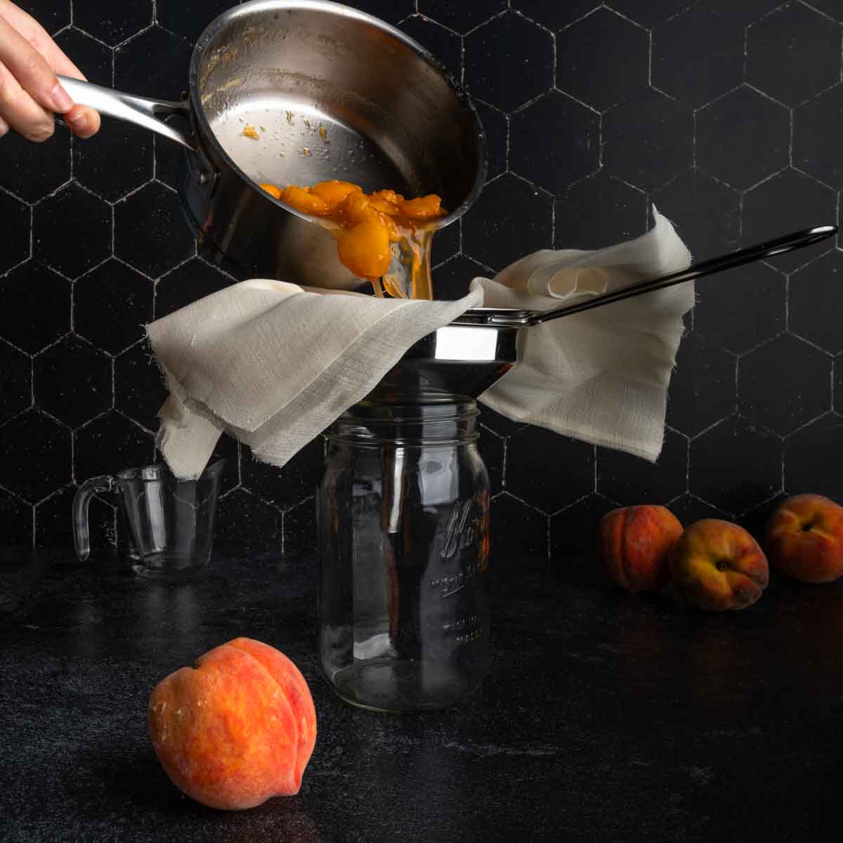 Pouring the peach syrup through cheesecloth and a funnel into a glass jar.