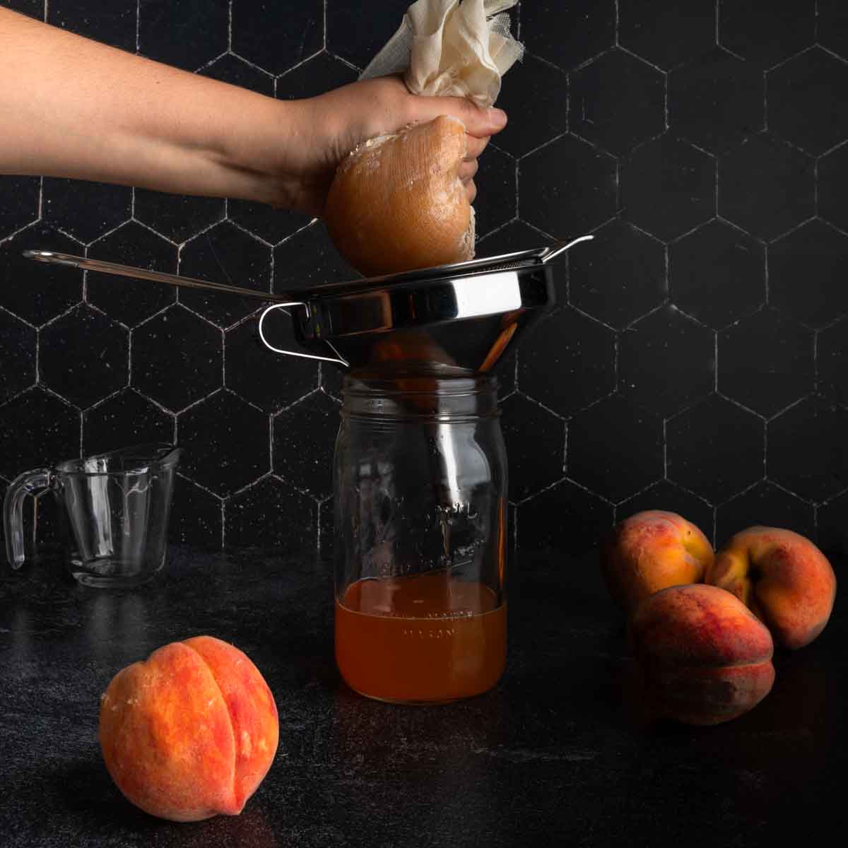 Squeezing the cheesecloth full of peaches over the jar of syrup.