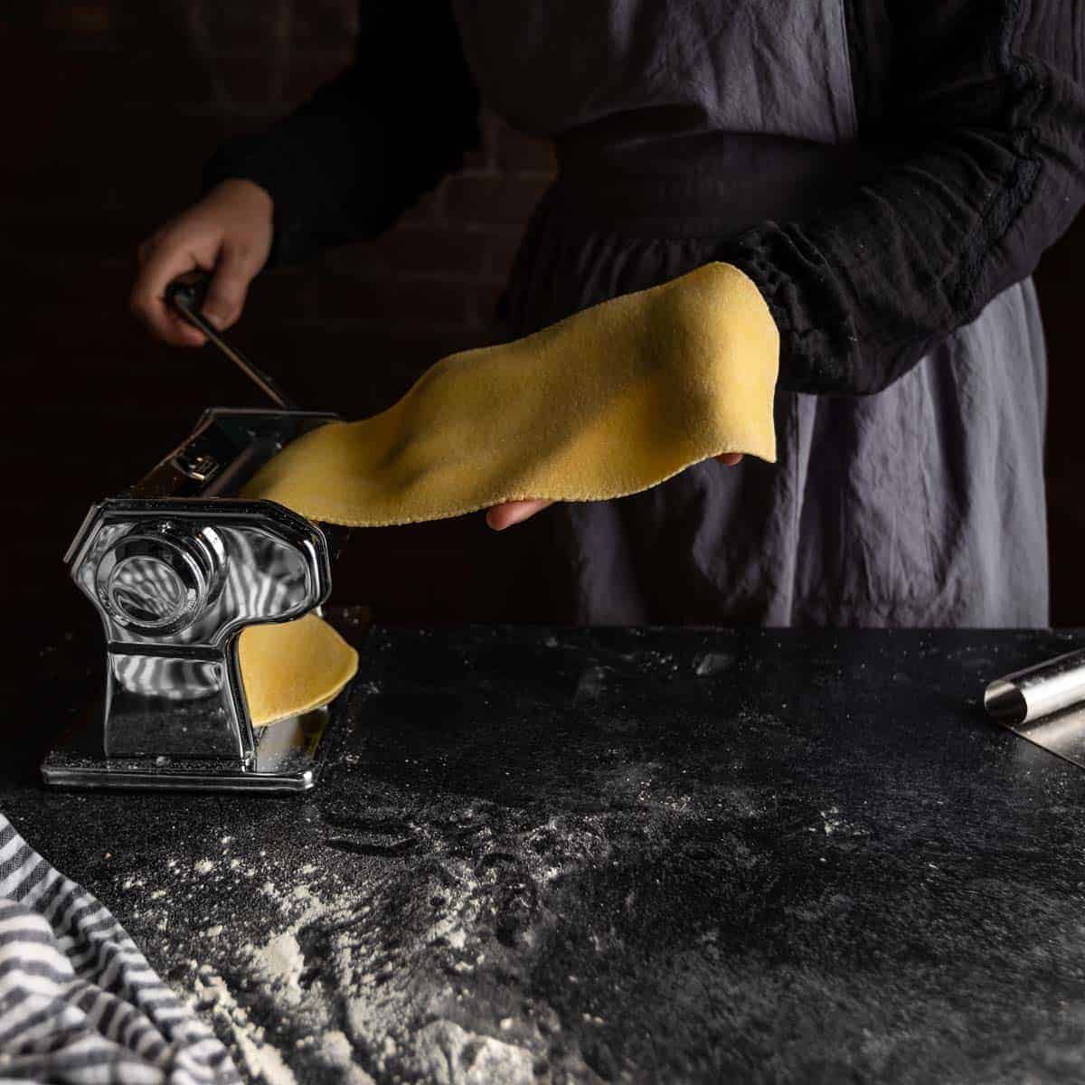 A woman running a sheet of pasta dough through a pasta machine