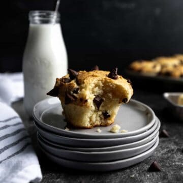 A chocolate chip muffin on a stack of plates, next to a jar of milk.