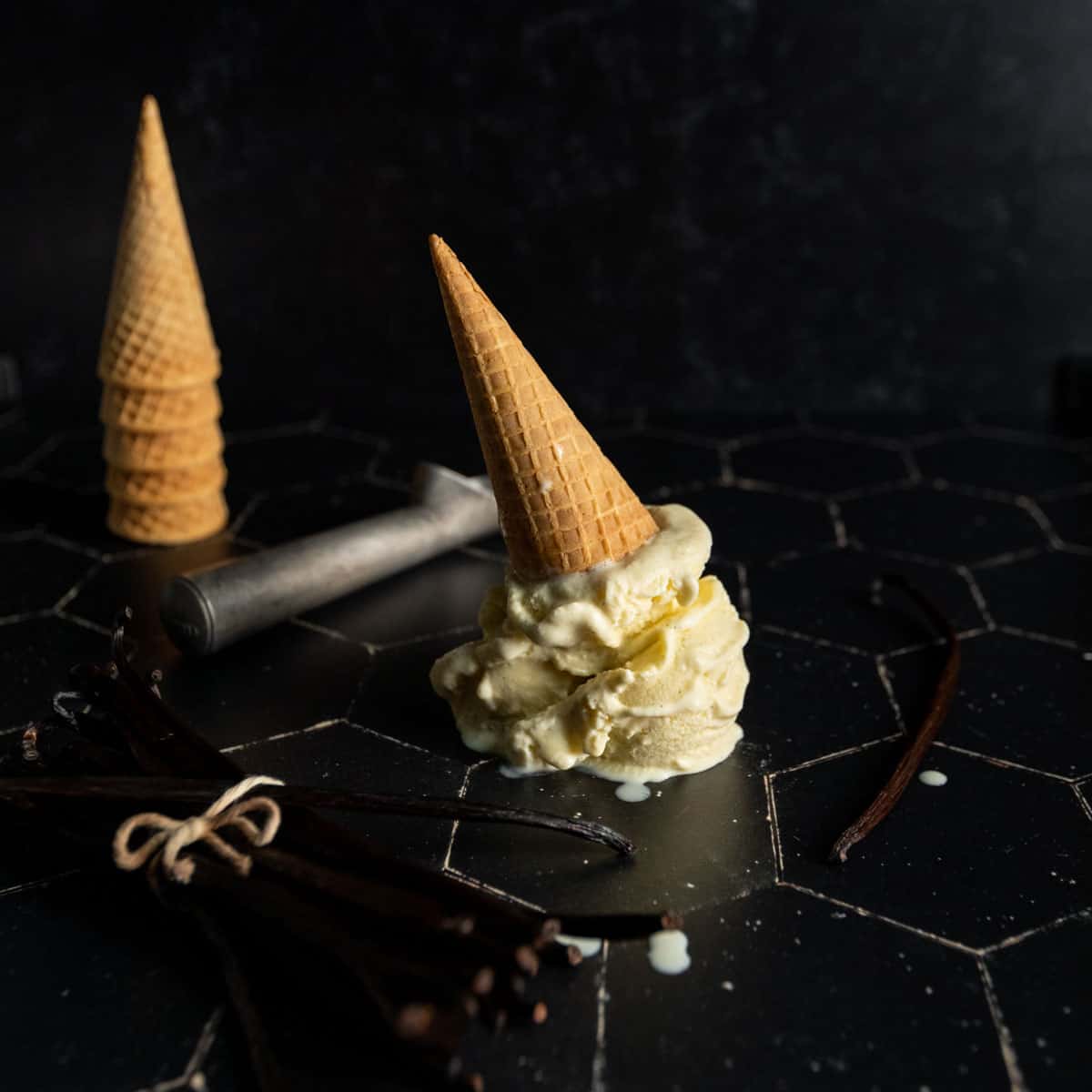 An upside-down ice cream cone with vanilla bean ice cream next to a scoop and stack of cones