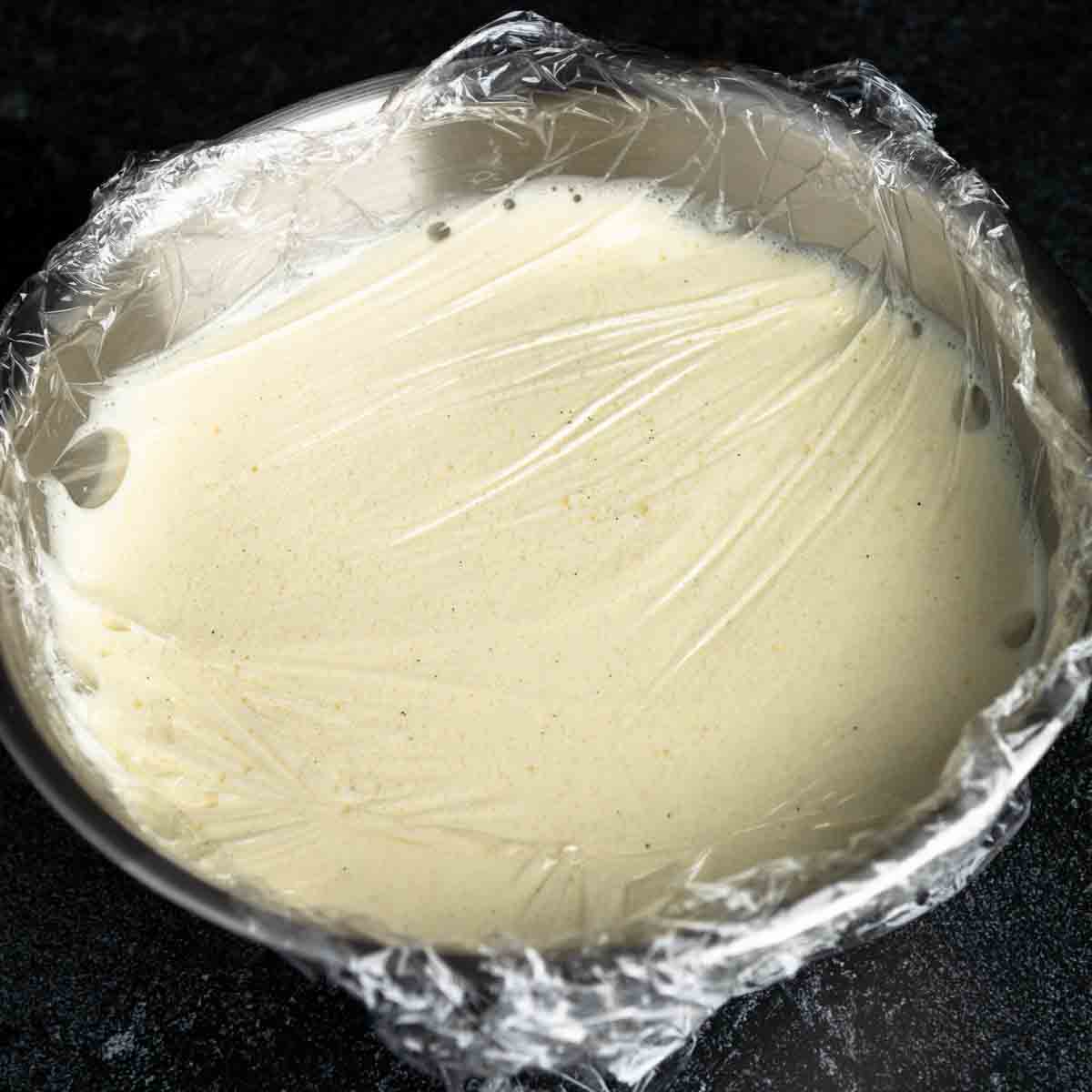 Vanilla bean ice cream base in a bowl covered with plastic wrap