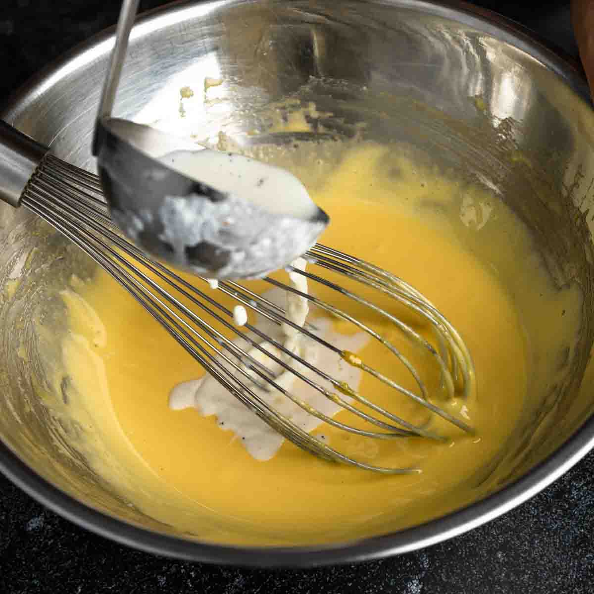 Ladling hot cream into the eggs to temper the custard
