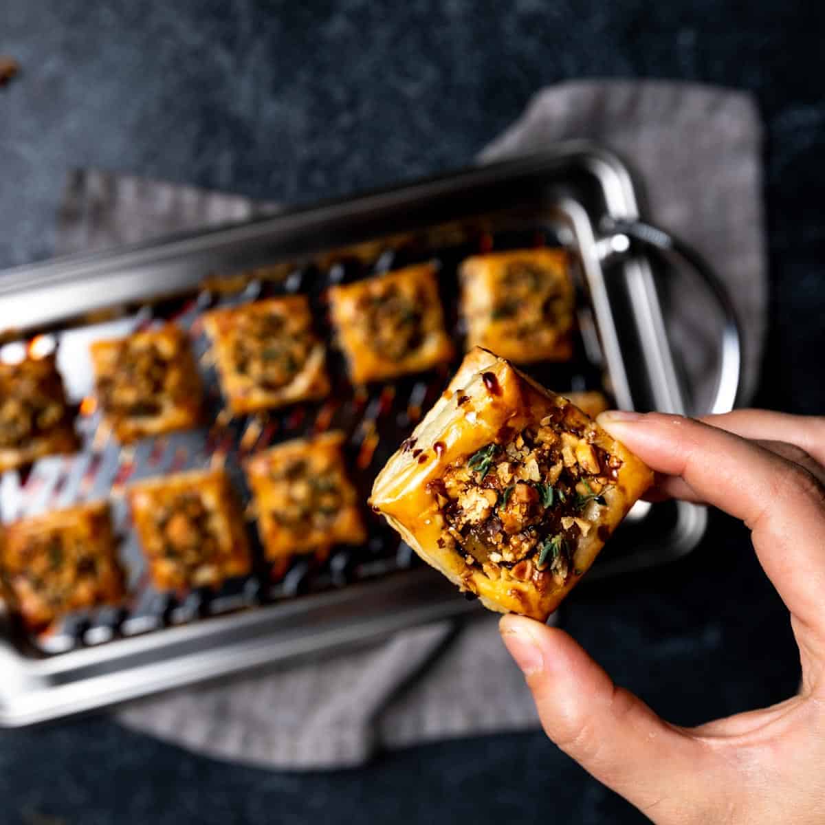 A hand holding a mini pear tart with a tray of more pear tartlets in the background