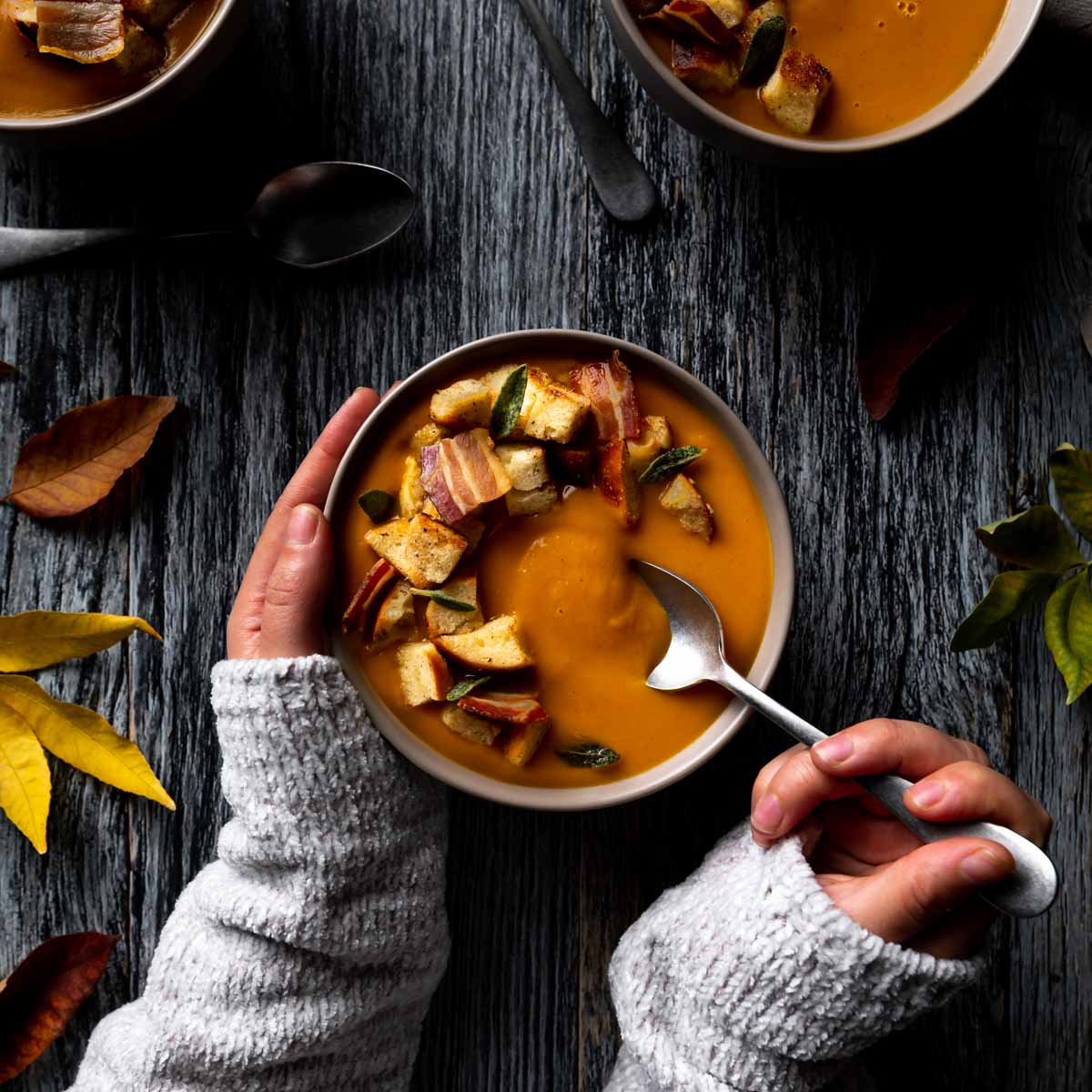 The first spoonful of sweet potato pumpkin soup being lifted from the bowl by sweltered hands.