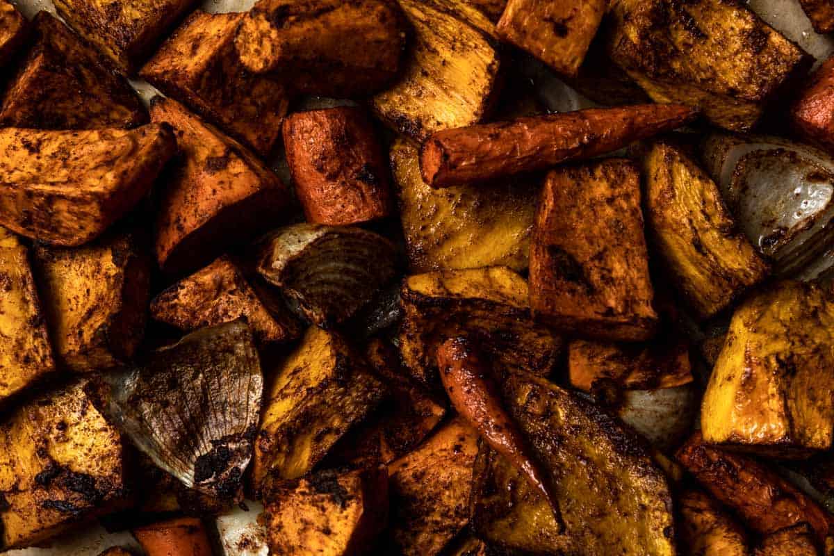 a close-up photo of roasted pumpkin, sweet potato, onion and celery on a sheet pan