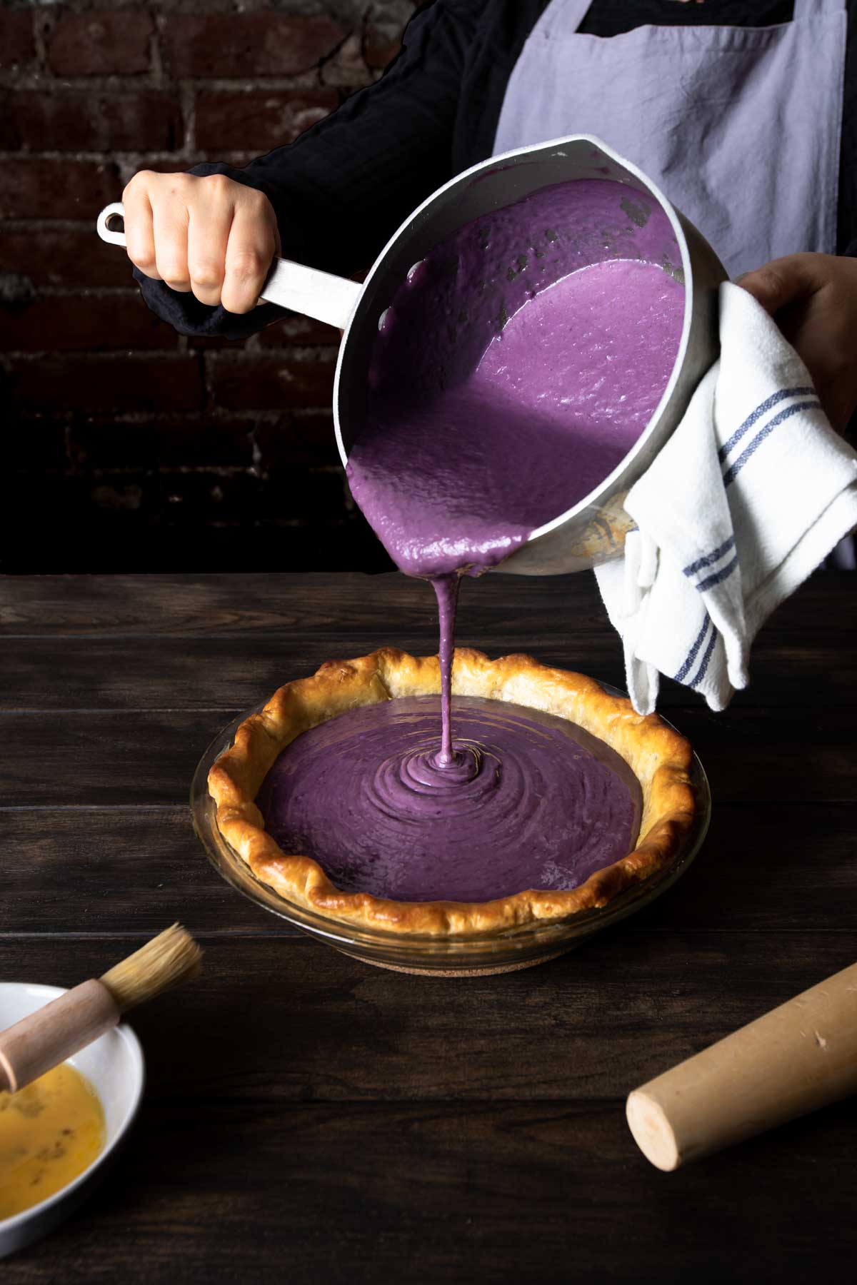 Purple sweet potato pie filling pouring from a pot into a baked pie shell