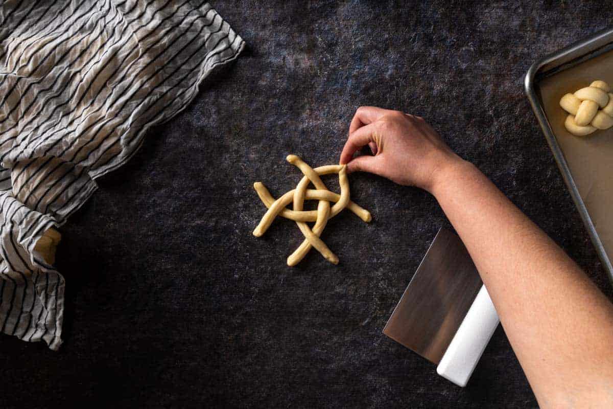 A hand pinching two of the adjacent strands of challah dough together.