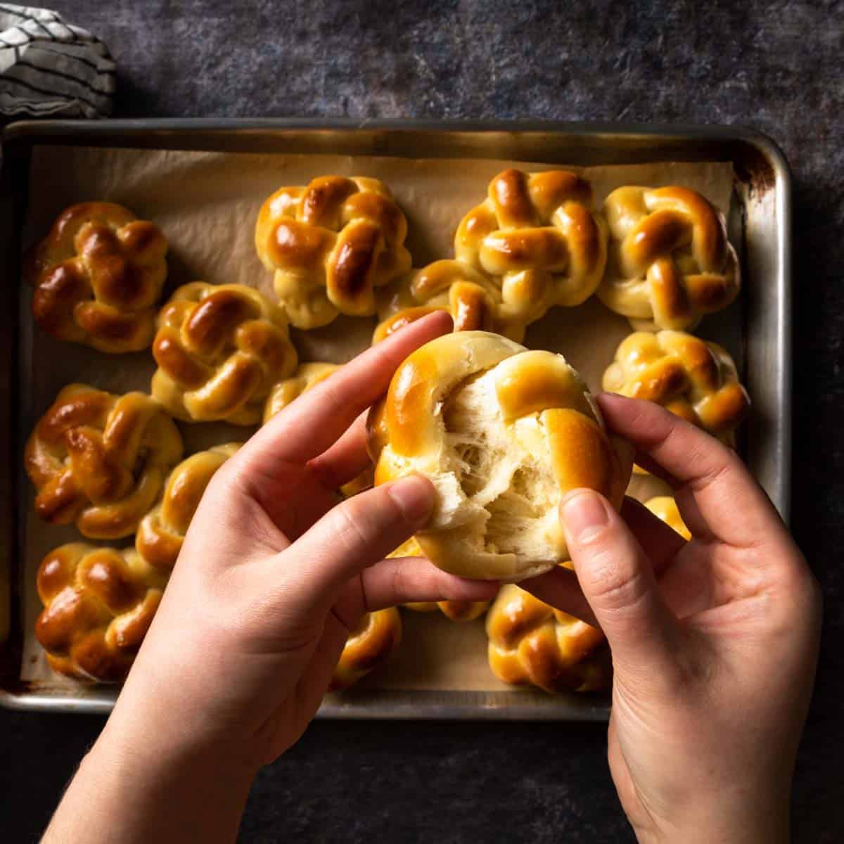 Hands breaking apart a fresh baked challah bun. 