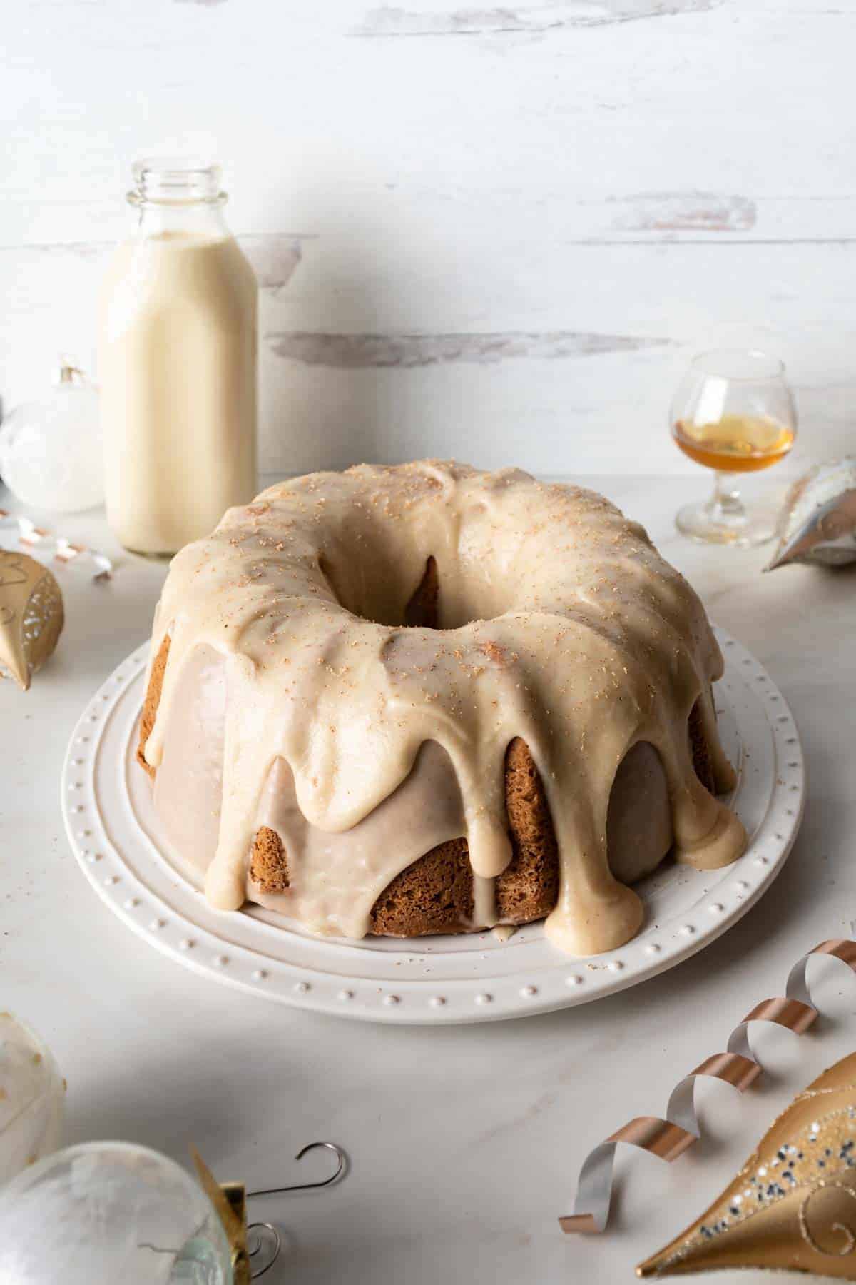 Eggnog Bundt Cake with rum eggnog frosting next to a jug of eggnog, glass or rum and Christmas ornaments